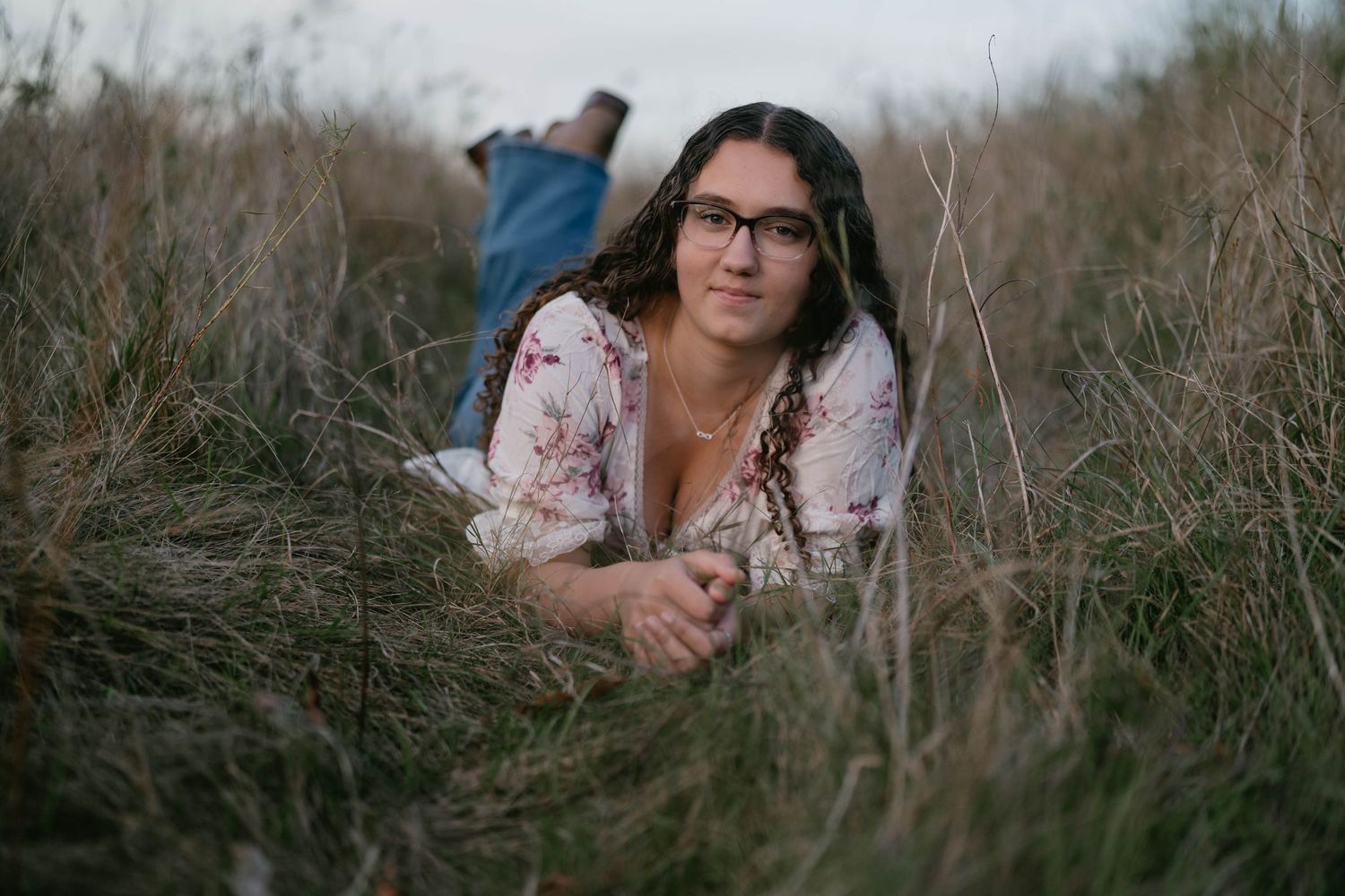 Senior standing in open grassy field at sunset, warm and dreamy portrait.