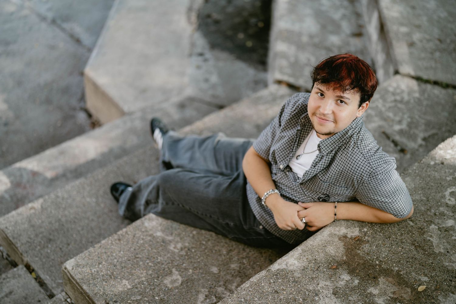 Senior portrait outdoors in parking lot, sitting on ledge with casual, joyful expression.