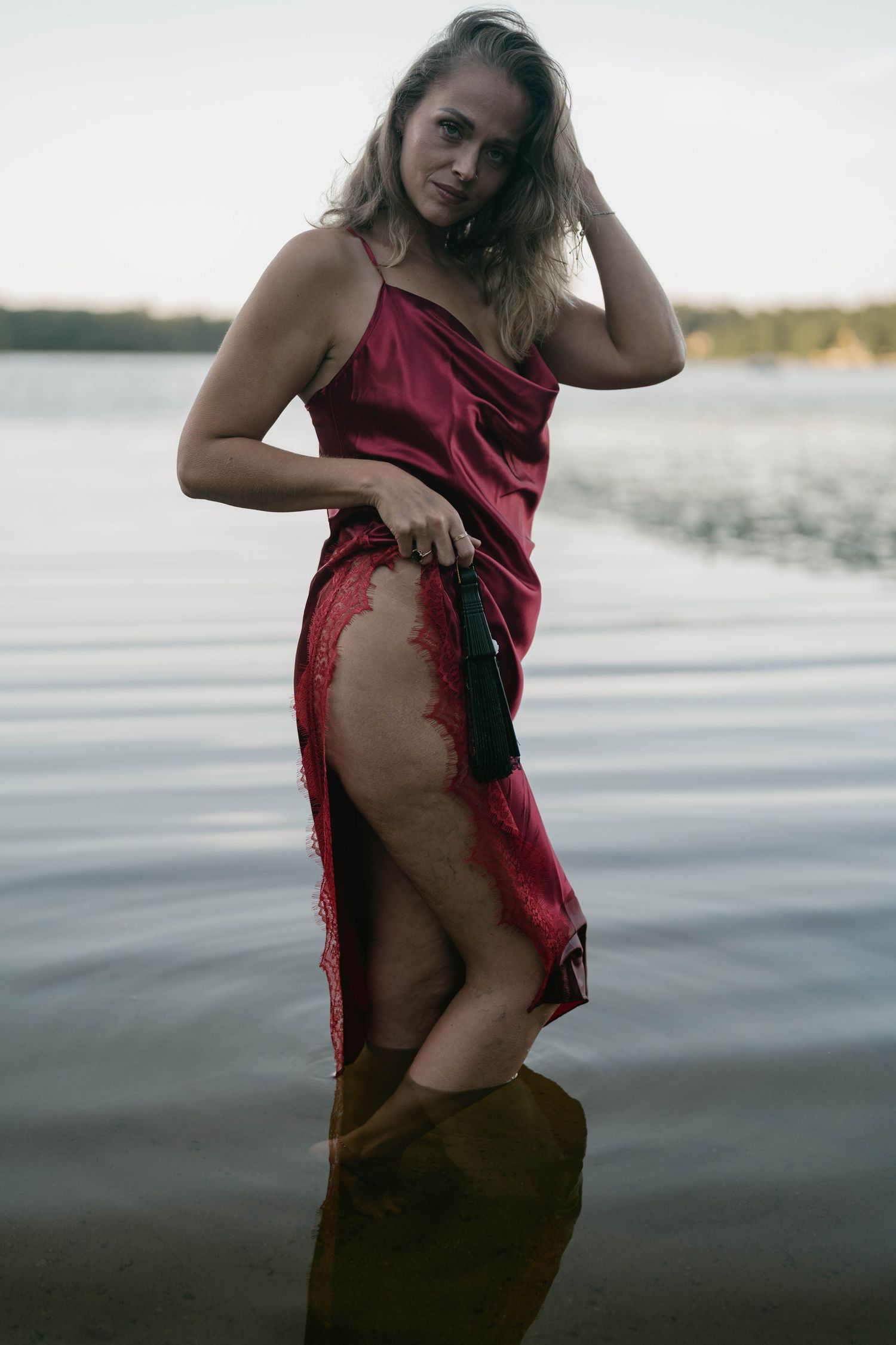 Moody lakeside photoshoot in burgundy dress with dramatic lighting.