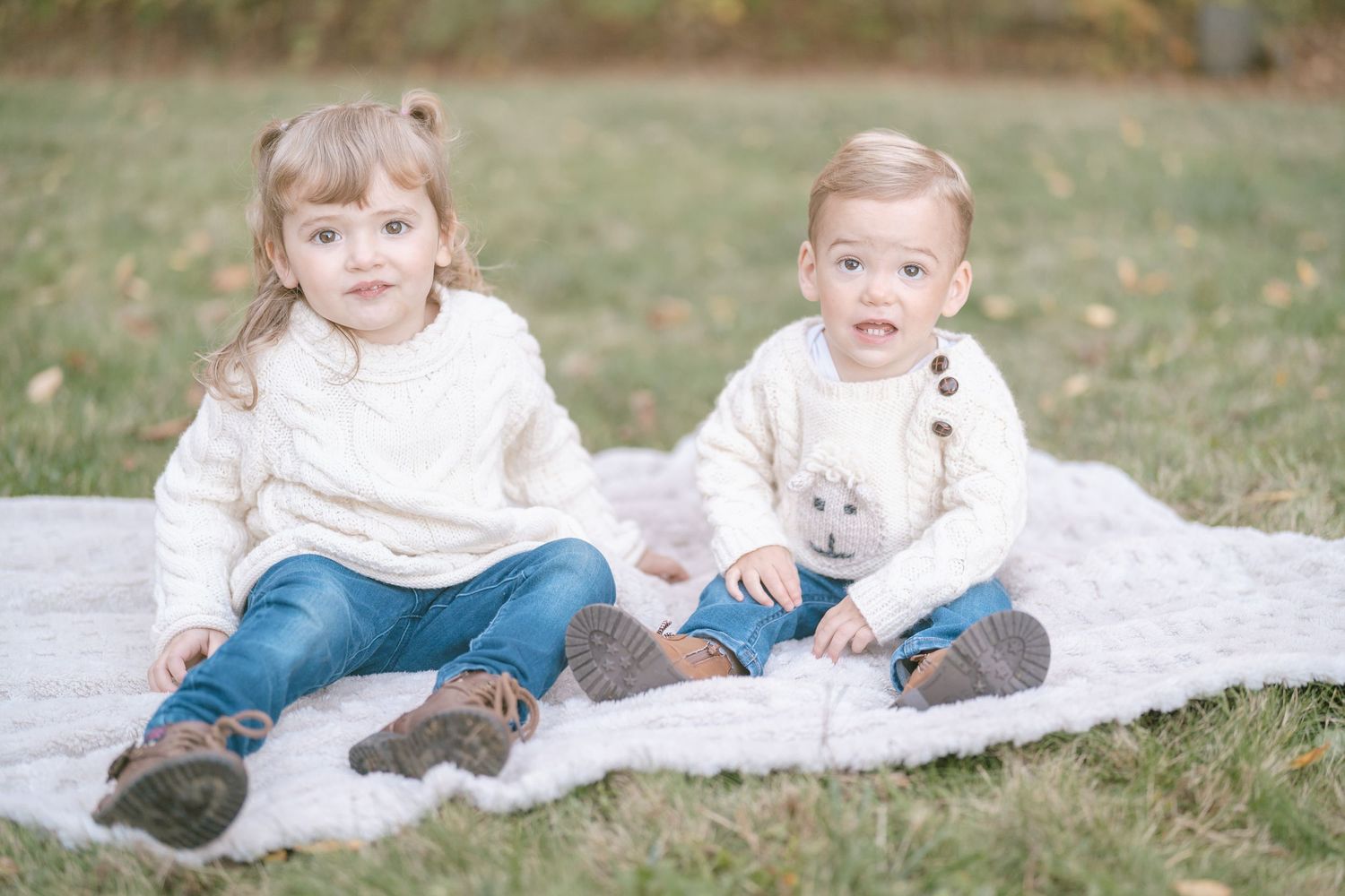 Children sitting together on a blanket in the grass during an autumn outdoor photo session.