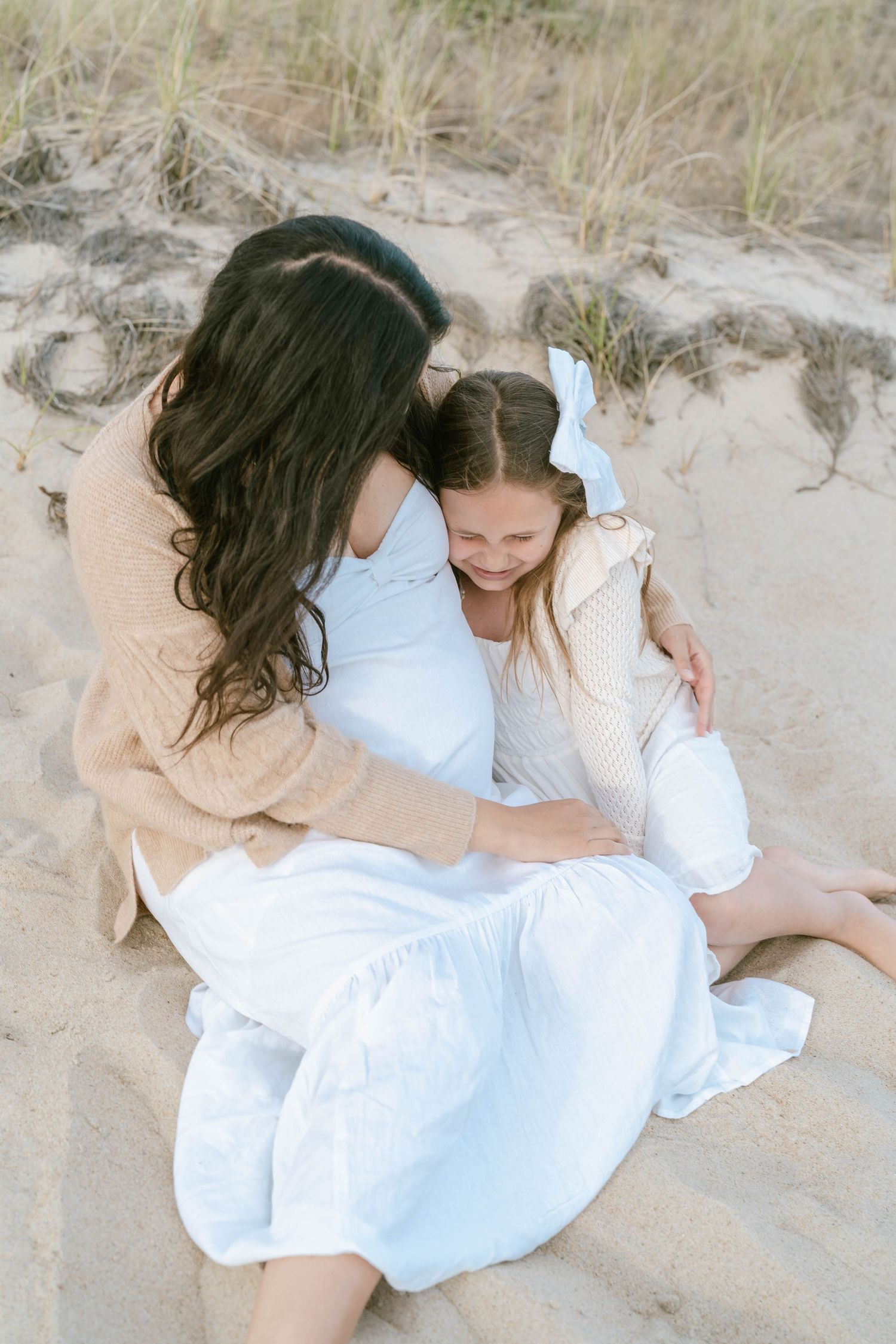 Two people in white dresses embracing on sandy beach dunes.
