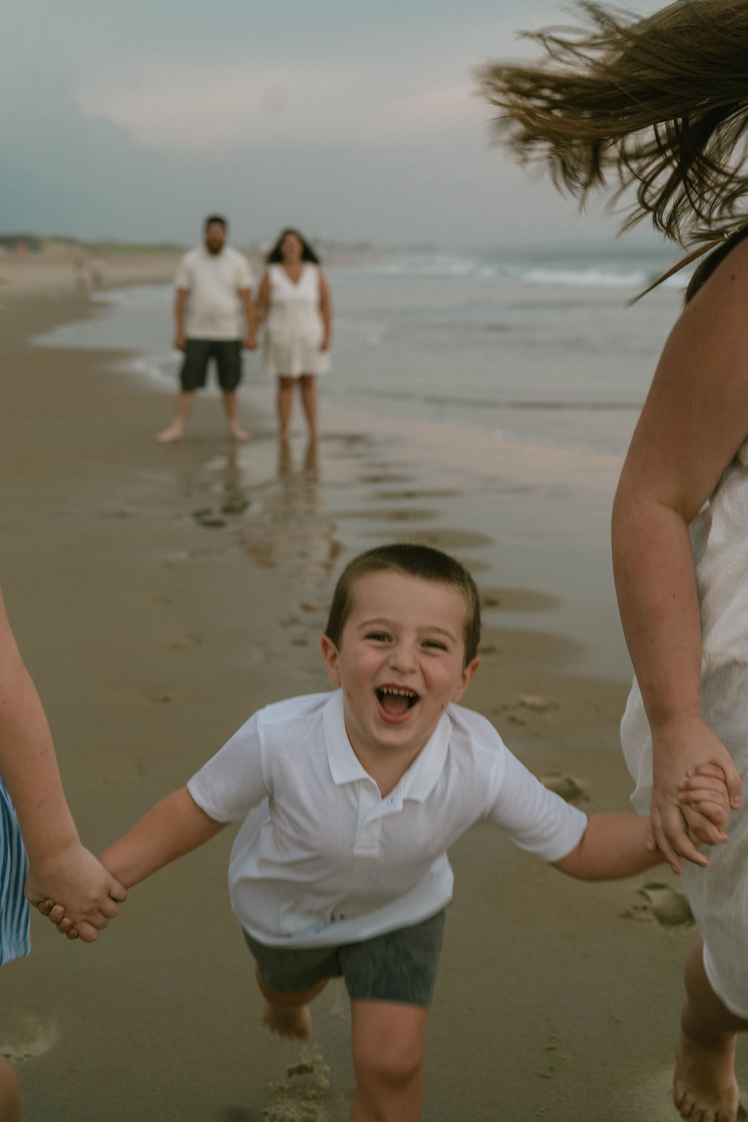 Family sitting on sand, smiling and enjoying a playful beach session.