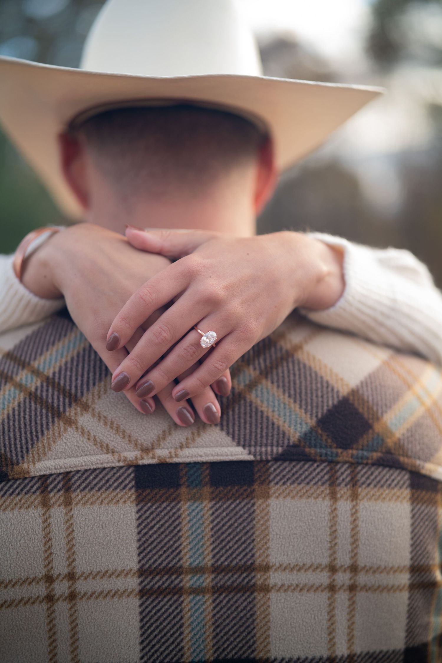 Close-up of hands wearing engagement ring resting on plaid blanket or fabric showing romantic moment.