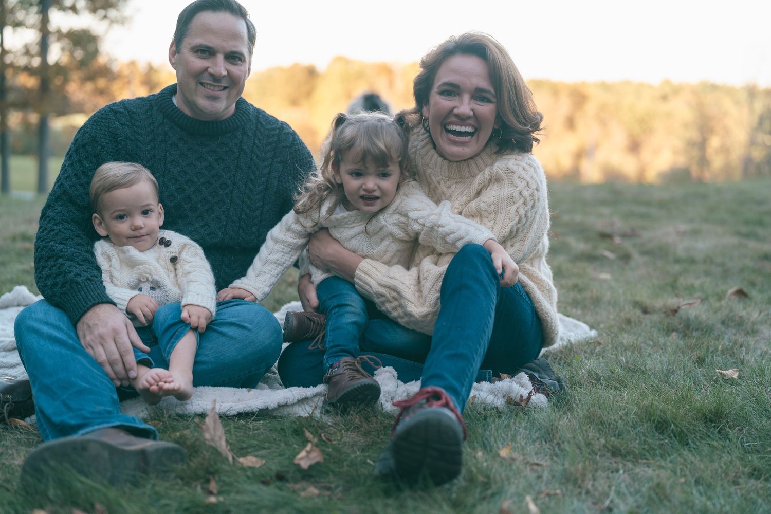 Family relaxing together on grass during golden hour sunset photo shoot.
