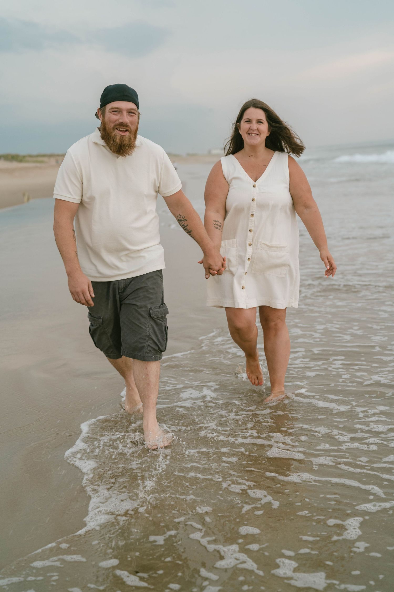 Two people holding hands and laughing as they walk along a peaceful, scenic beach.