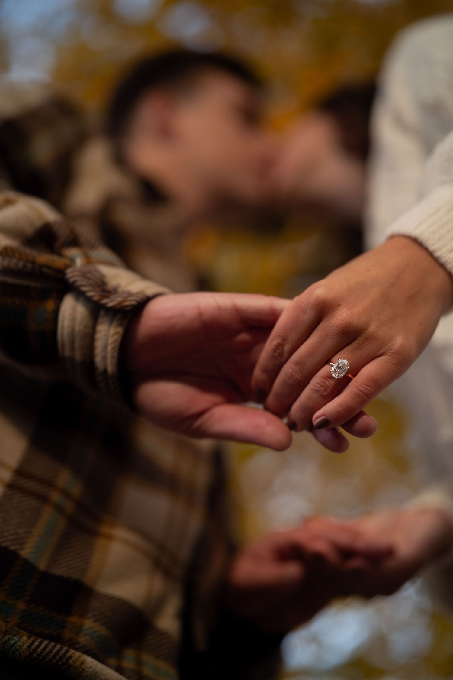 Close-up of hands showing off a sparkling engagement ring during an autumn proposal moment.