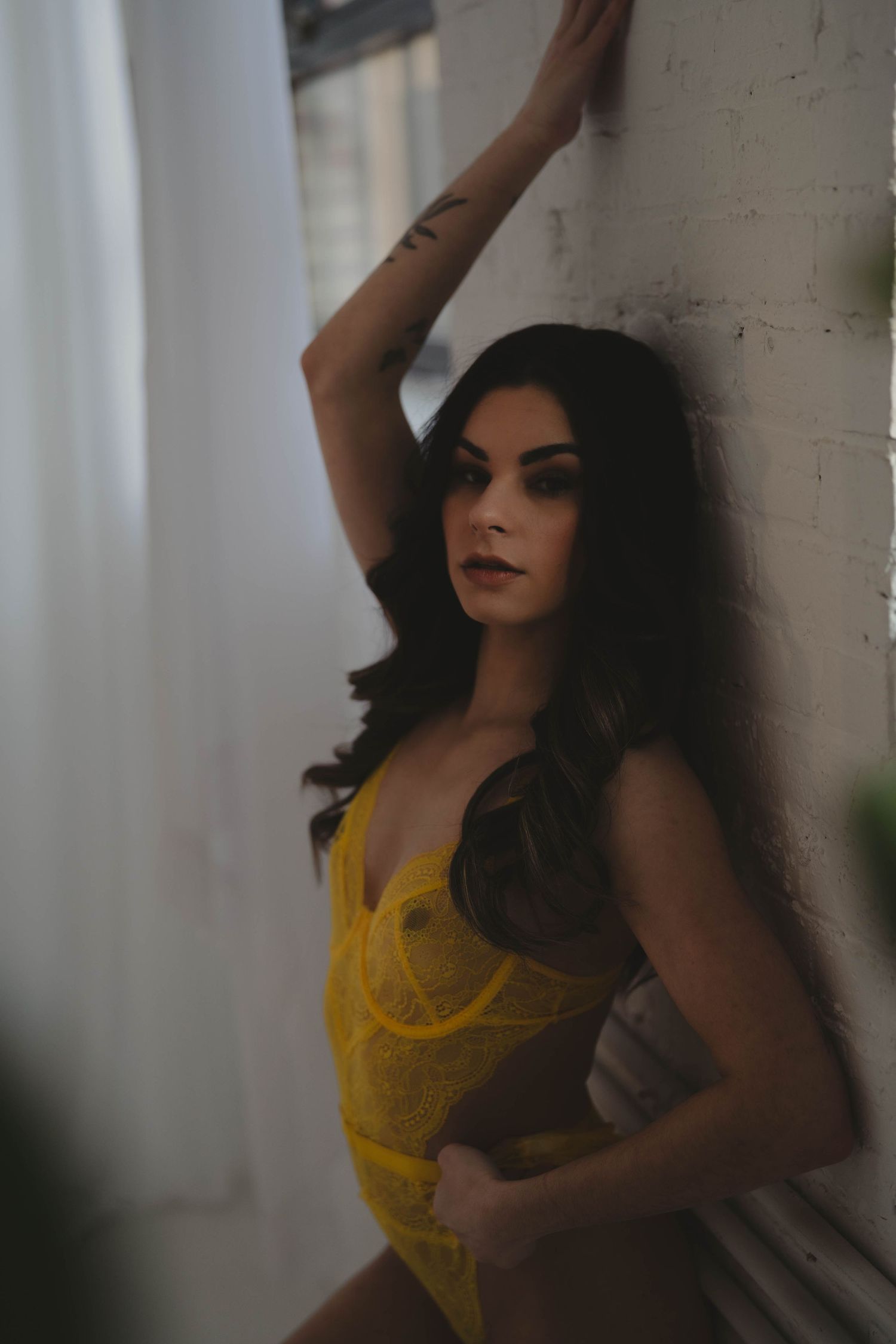 Moody portrait series against white brick wall in yellow lingerie.