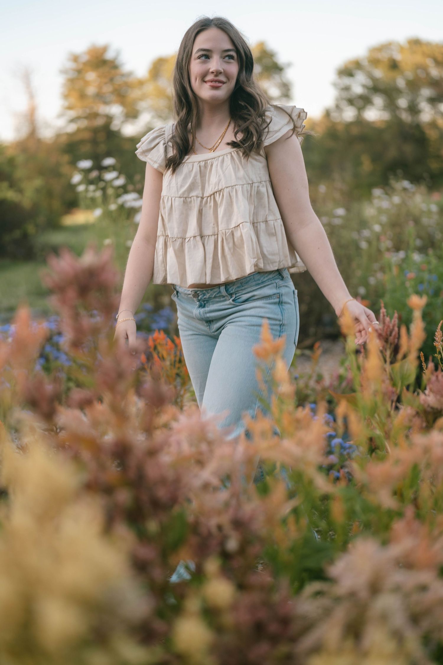 Teen standing with arms outstretched in a blooming field, light and airy portrait.