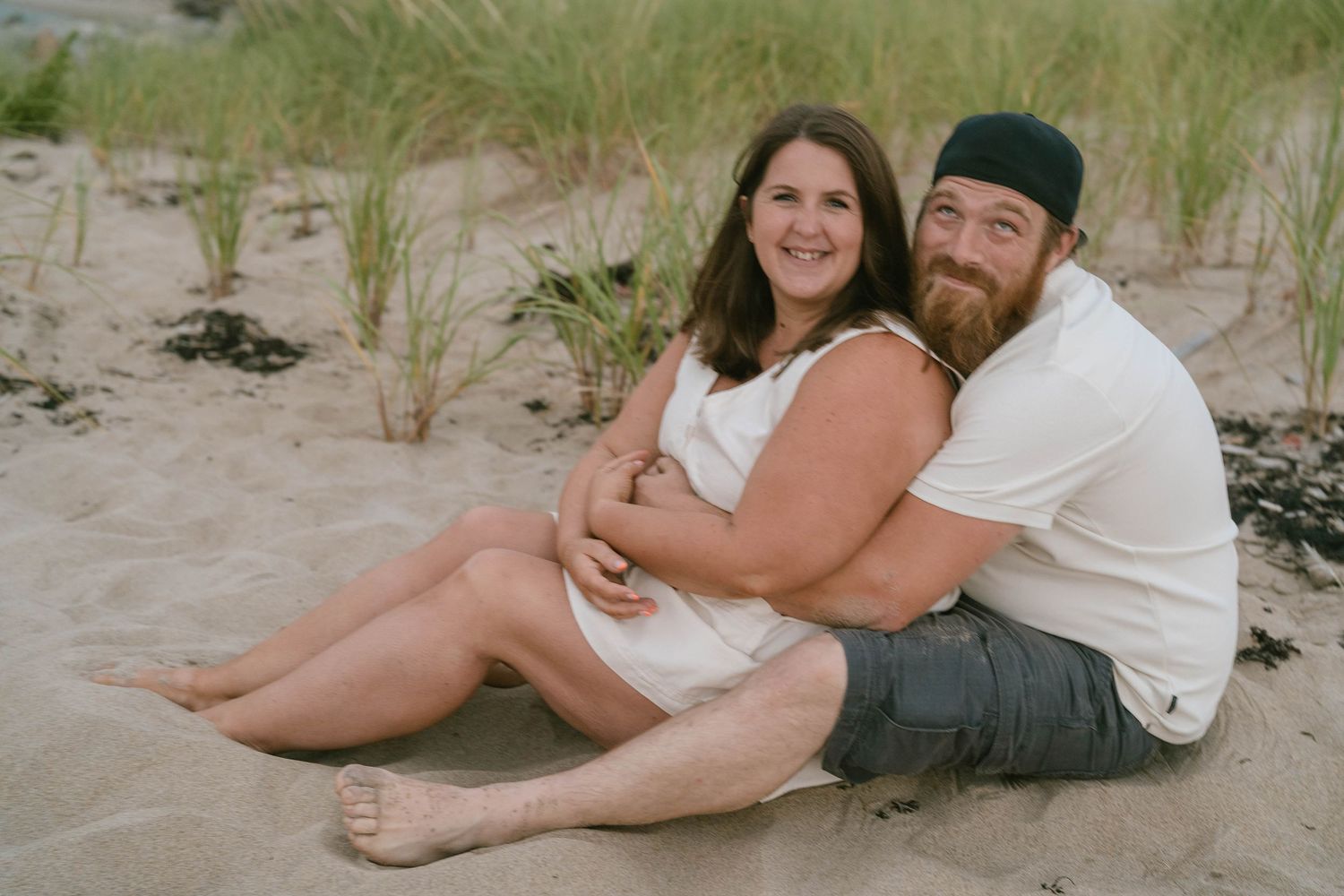 Couple embracing by the water on a sunny beach day, capturing a natural, happy moment.