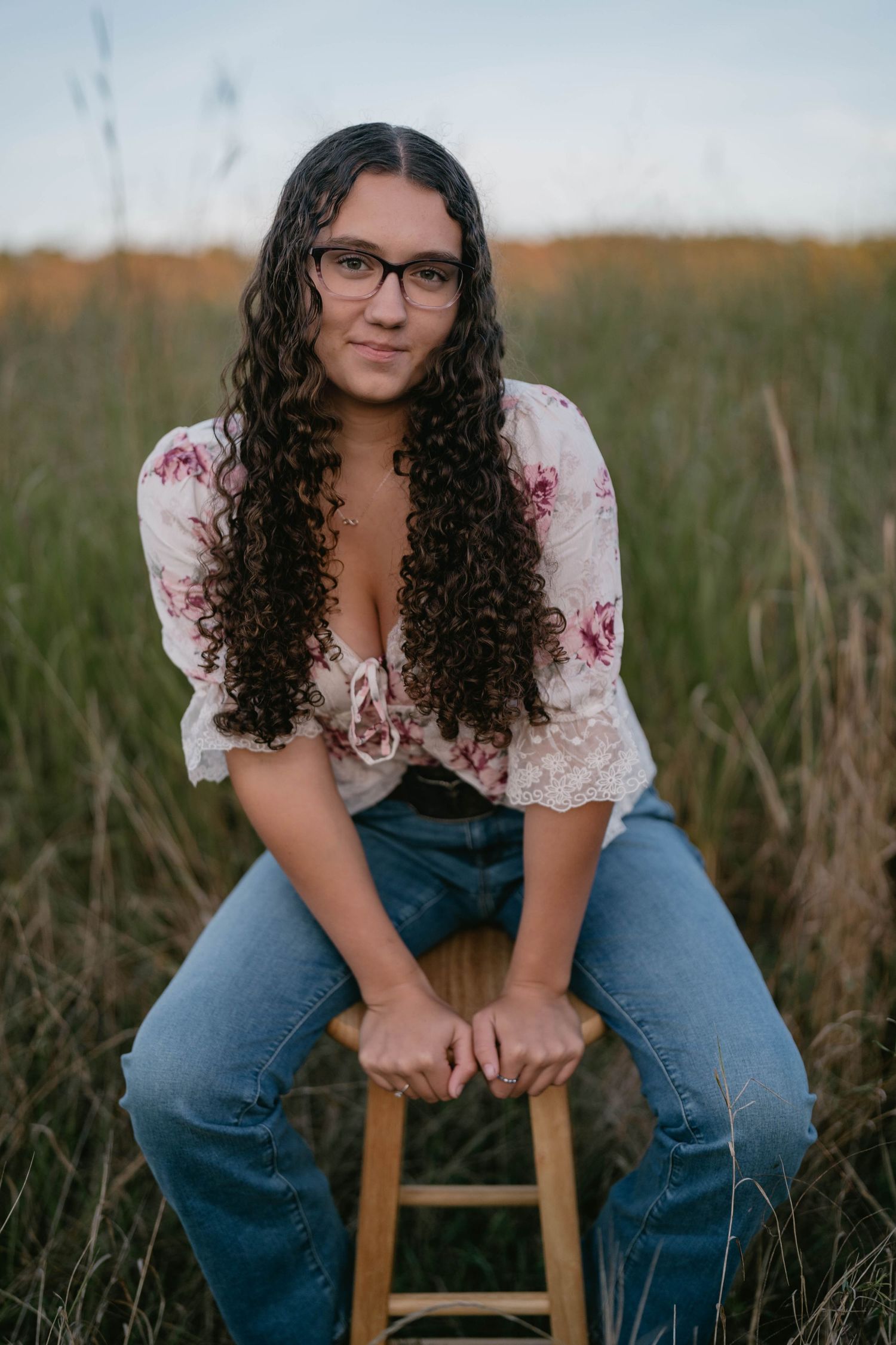 Senior standing in open grassy field at sunset, warm and dreamy portrait.