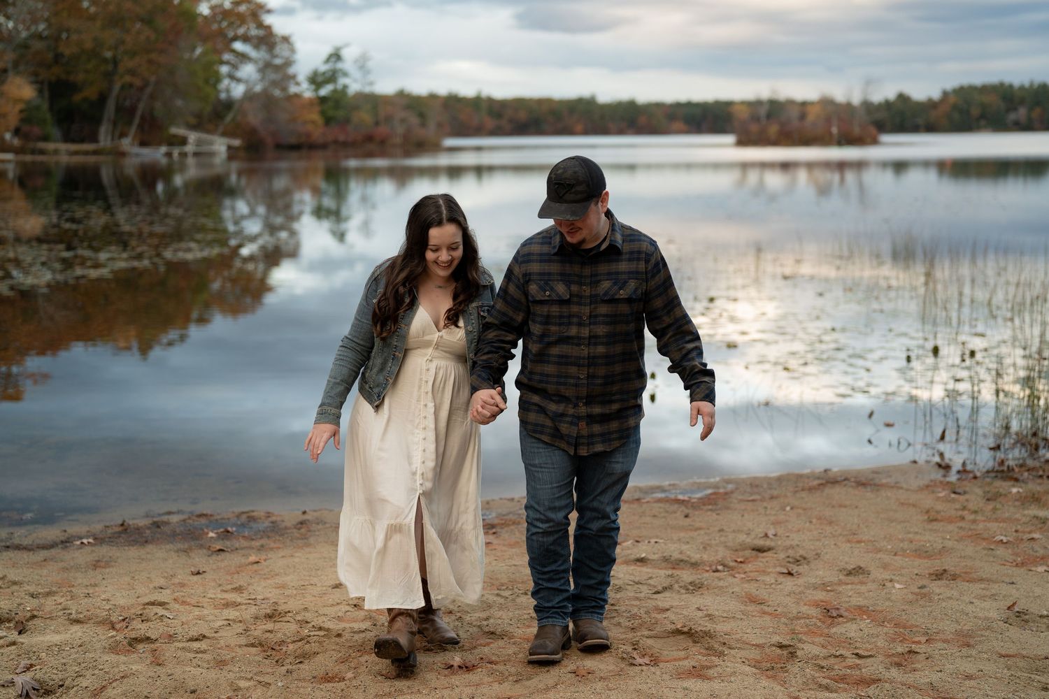 Couple walking together on sandy beach shore during autumn sunset.