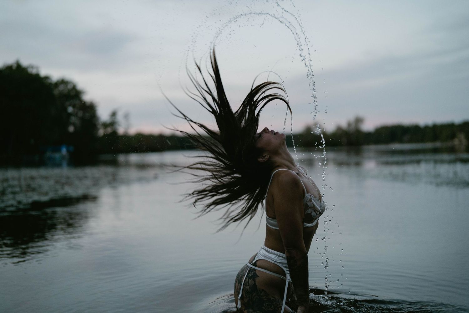 Artistic water photoshoot with splashing droplets and dramatic movement against a moody lake backdrop.