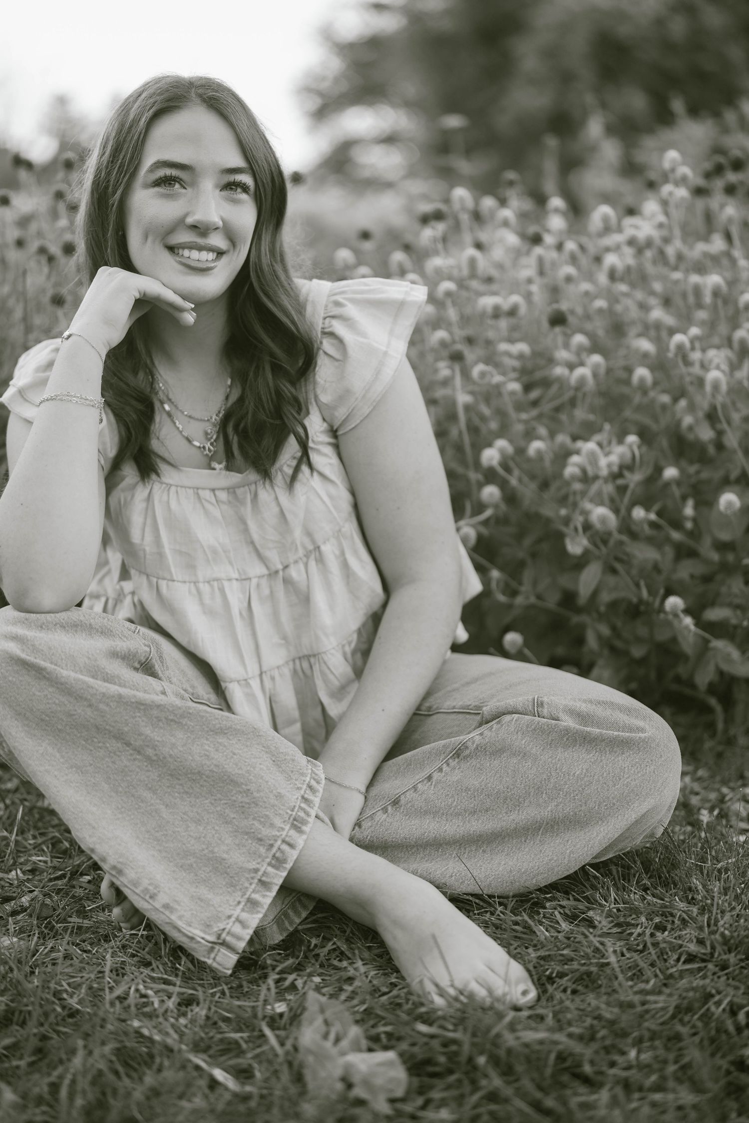 Black and white portrait of woman in denim lounging among wildflowers.