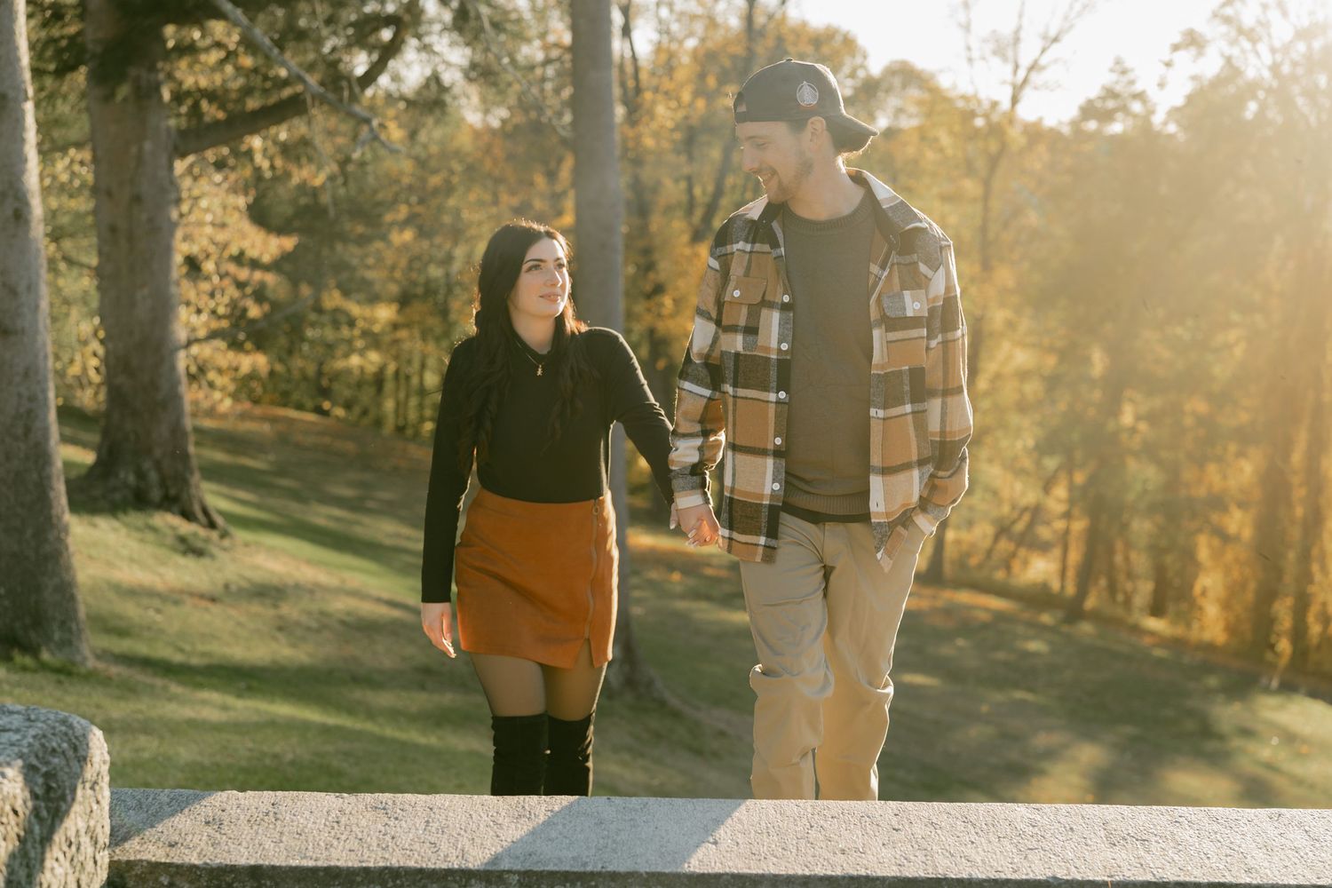 A couple walks together during golden hour in a scenic autumn park setting.