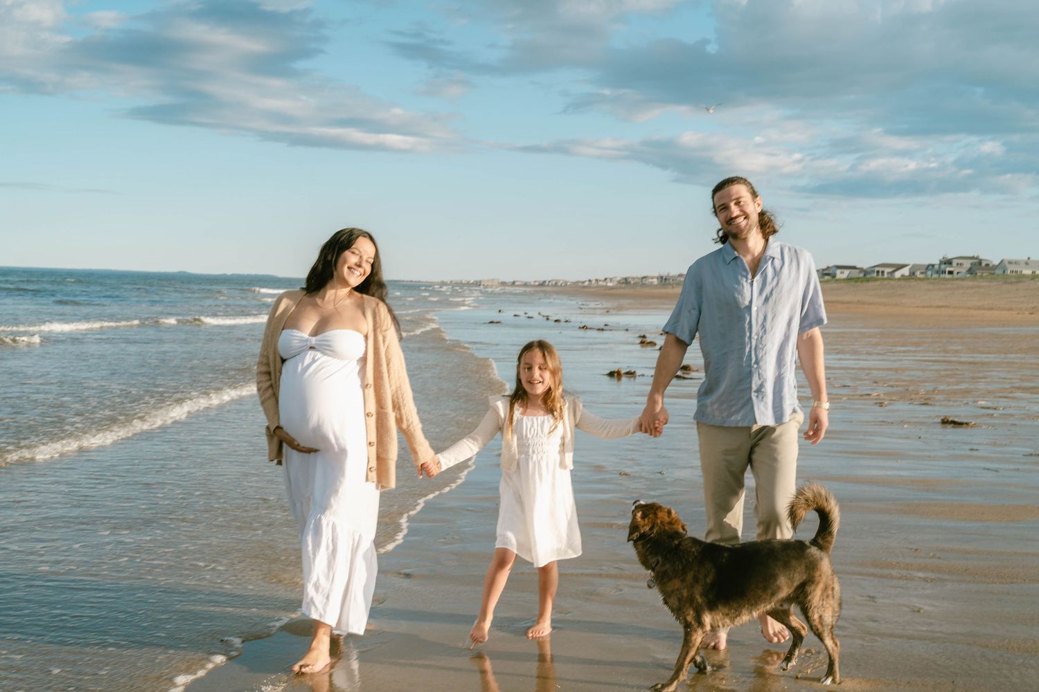 A family walks along the shoreline with their dog as waves roll in.