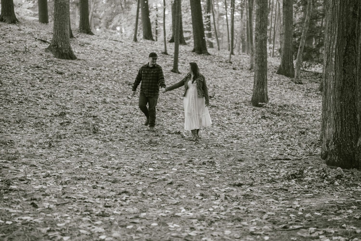 Couple walking through a forest path covered in fallen autumn leaves.