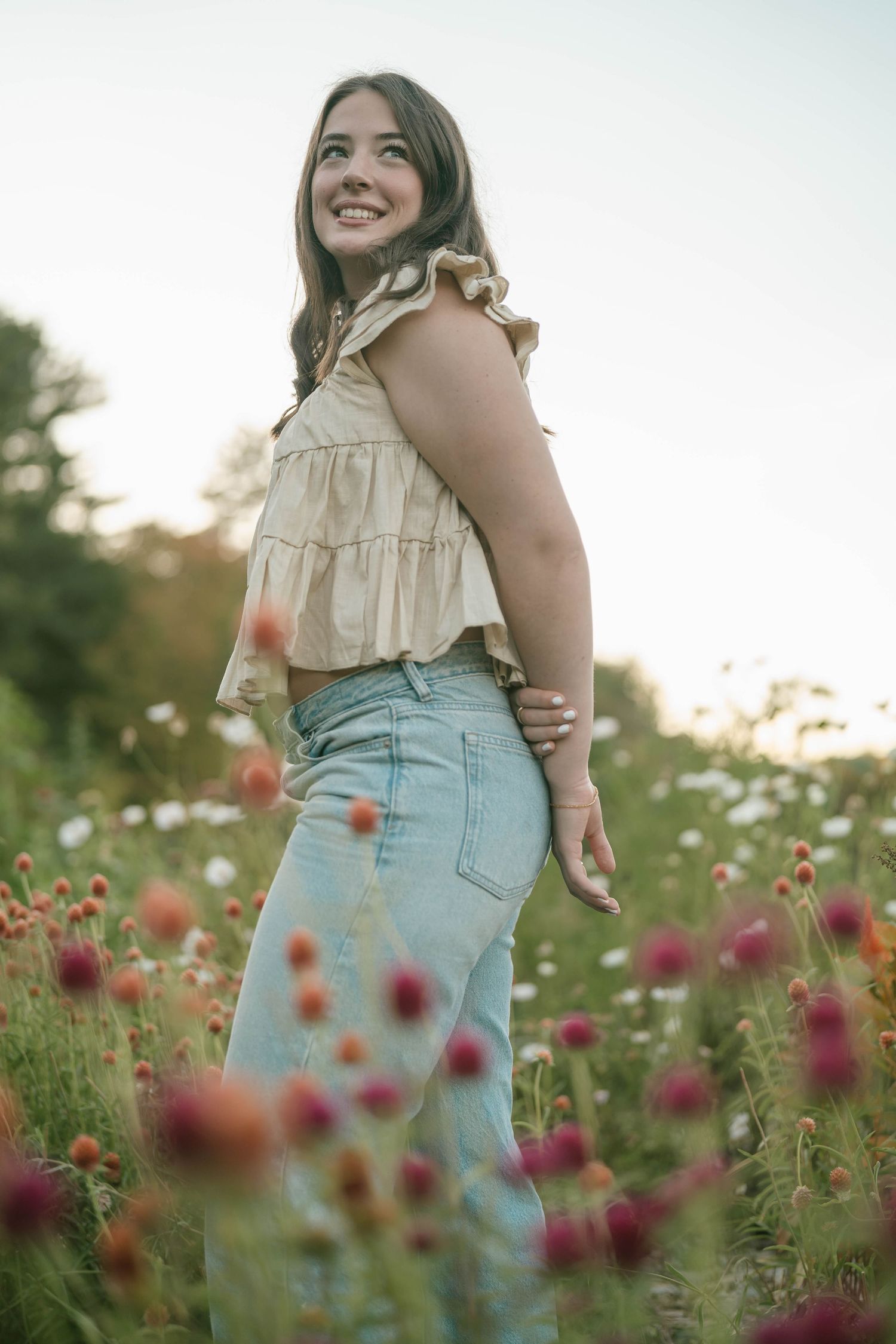 Teen standing with arms outstretched in a blooming field, light and airy portrait.