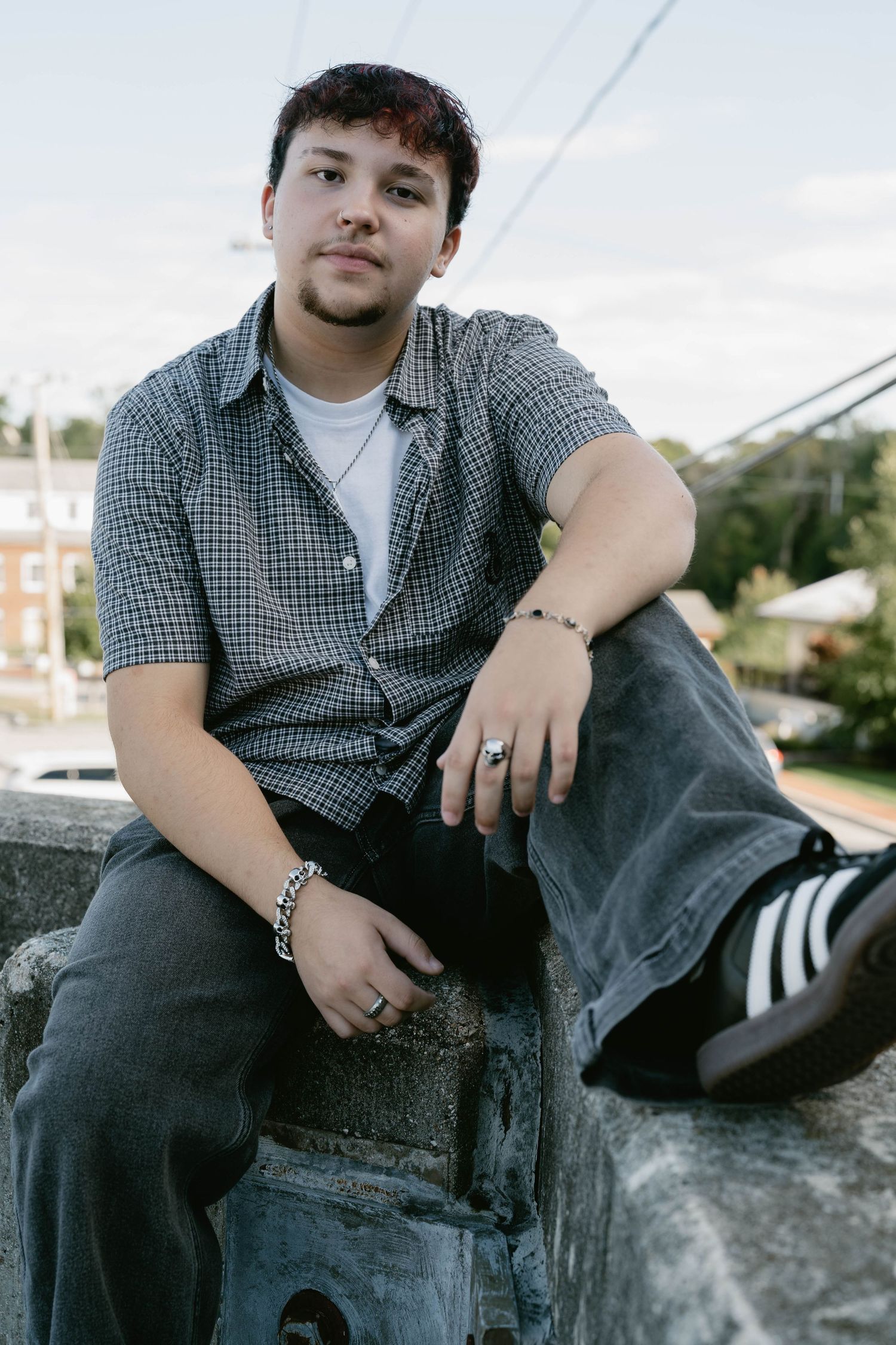Teen posing casually on concrete ledge in parking lot, captured in natural, candid lig