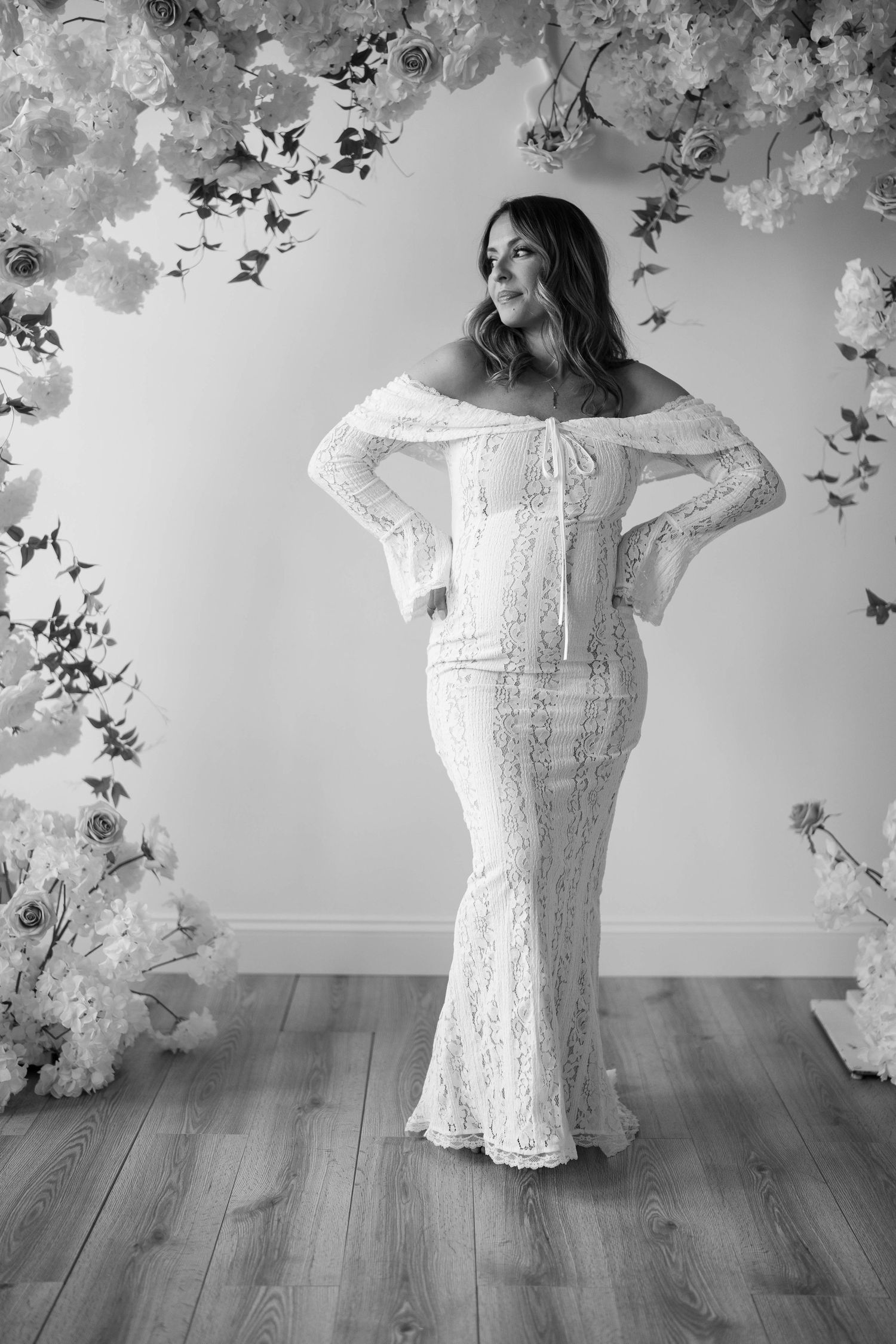 Dramatic black and white maternity portrait with floral arch and lace gown.