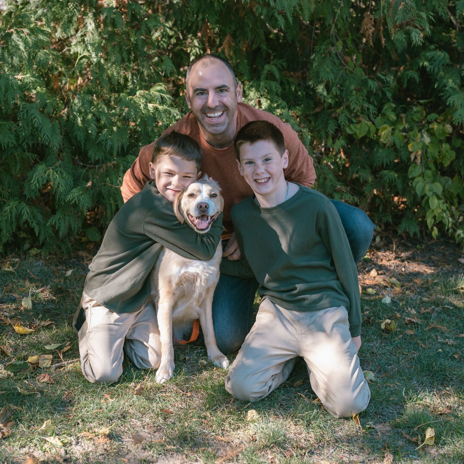 Playful family photo session with a dog in a leafy green outdoor setting.