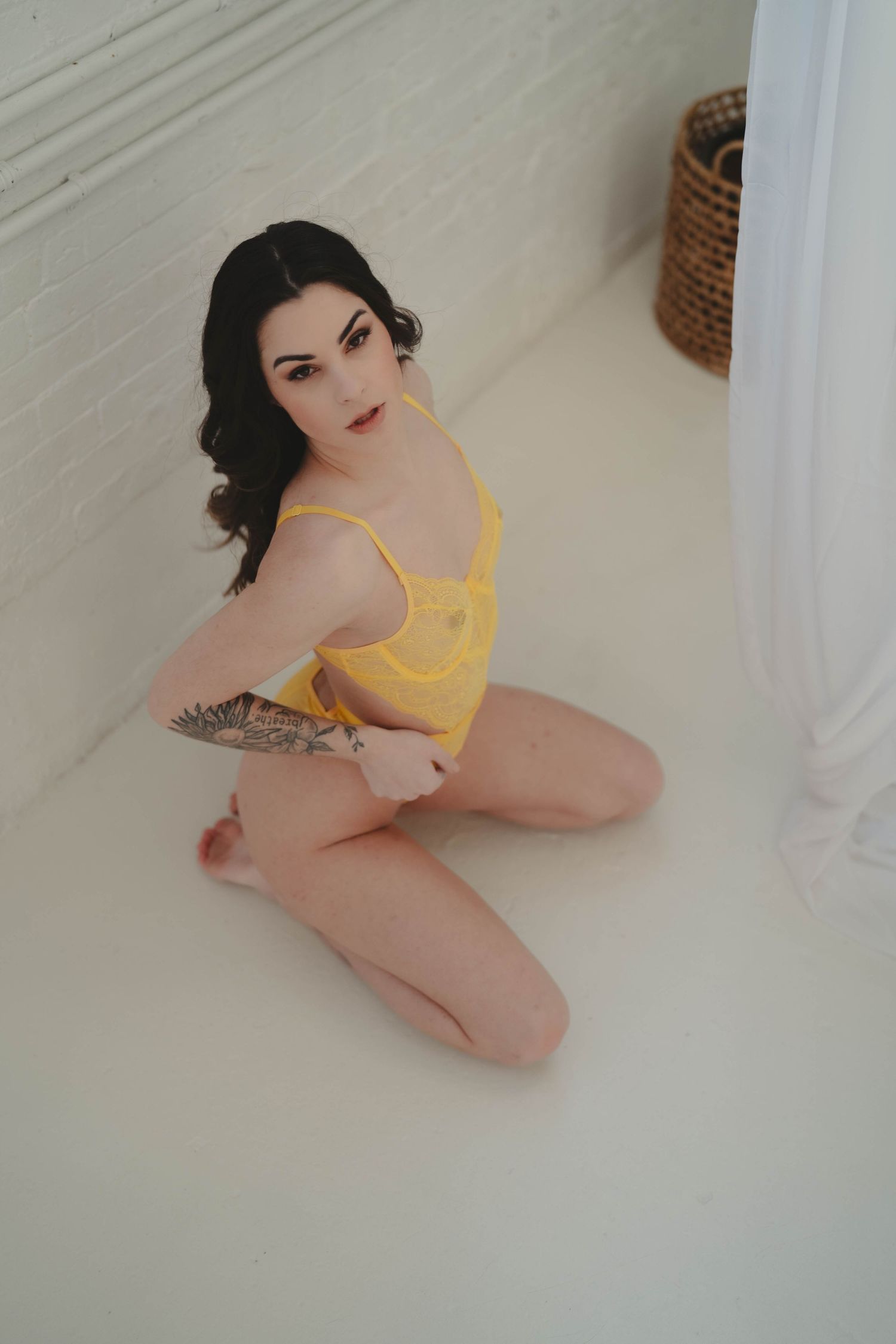 Minimalist boudoir photography with yellow lingerie on white floor.