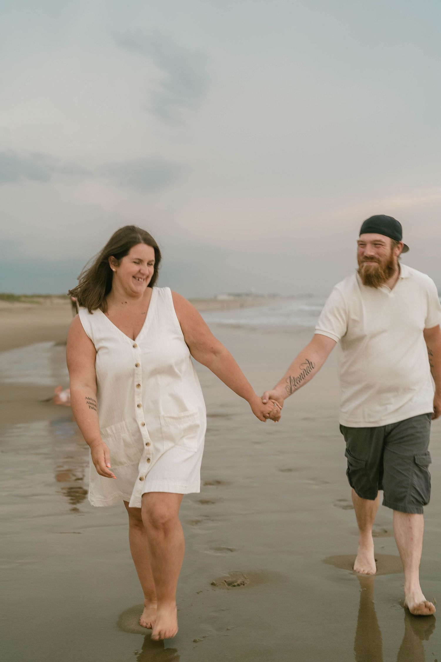 Partners walking along the shoreline with waves behind them, sharing a joyful, intimate beach session.