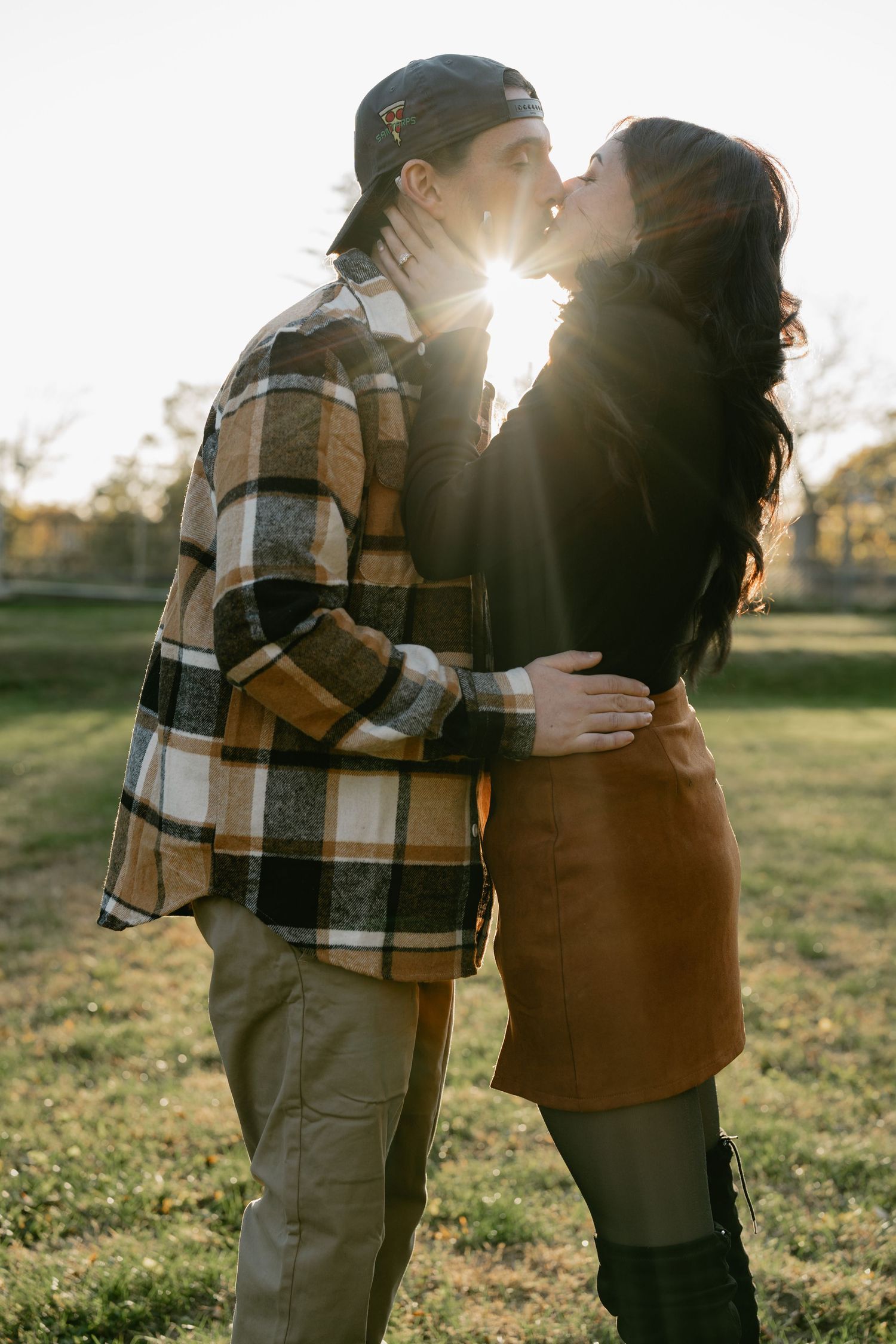 A romantic couple embraces in a sunlit field while wearing casual fall clothing on an autumn afternoon.