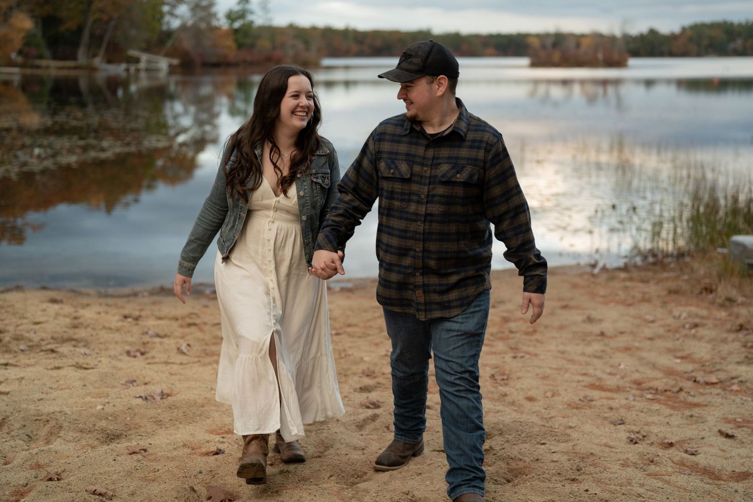 Happy couple strolling along lakeside beach during cloudy autumn day.