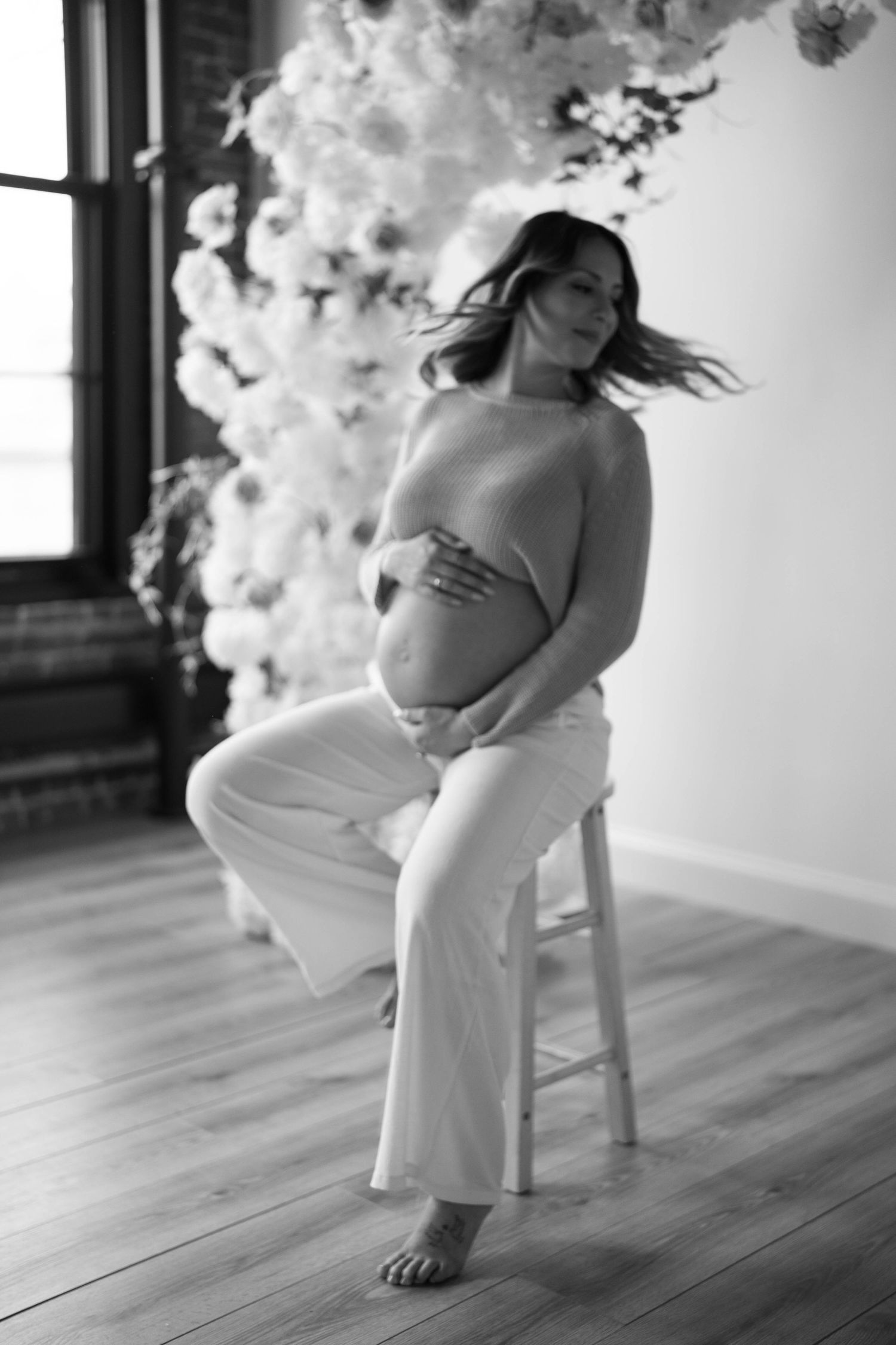 Artistic black and white maternity photo with flowing white gown and floral backdrop.