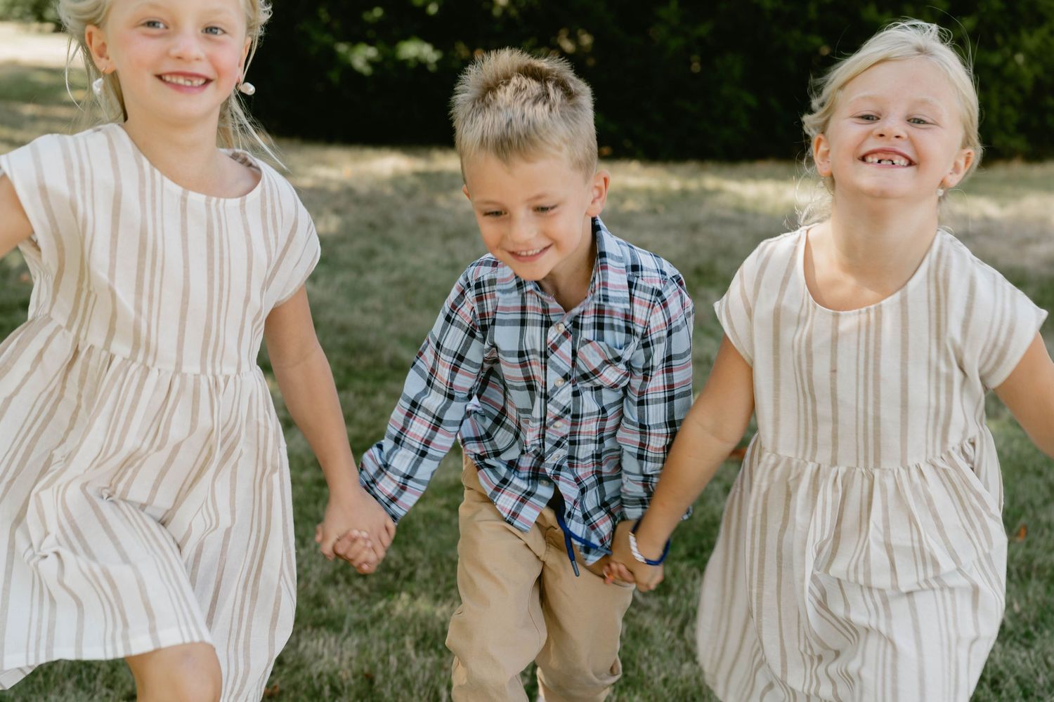 Children sitting together wearing coordinated white and plaid outfits for outdoor photos.
