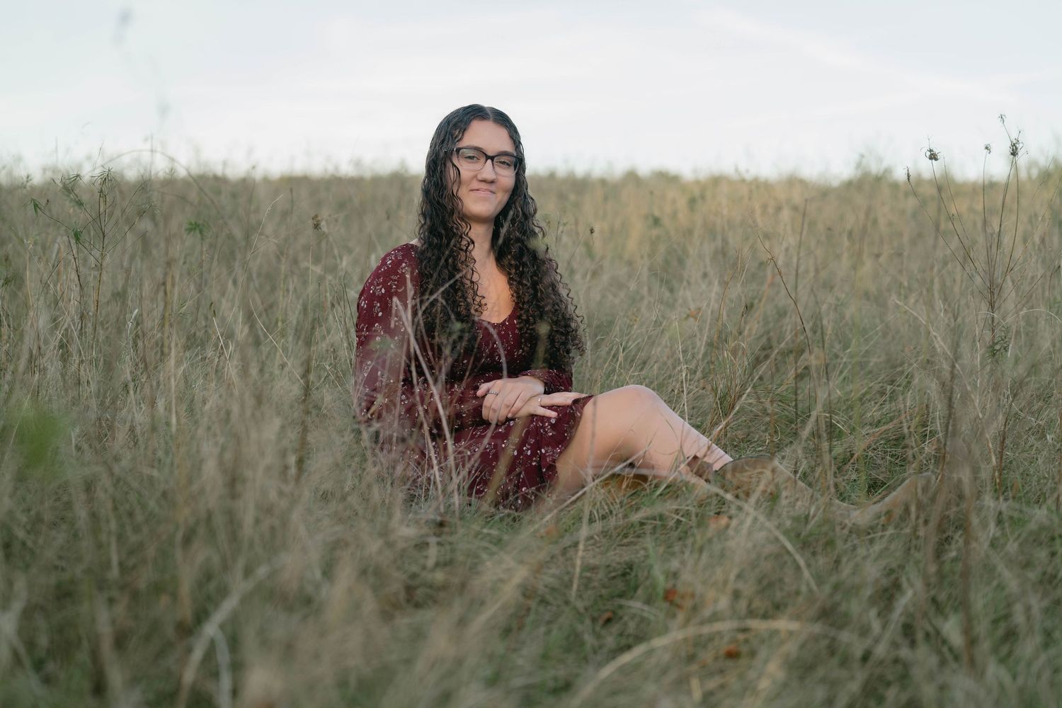 Teen crouching in grass, casual senior portrait with warm sunlight.