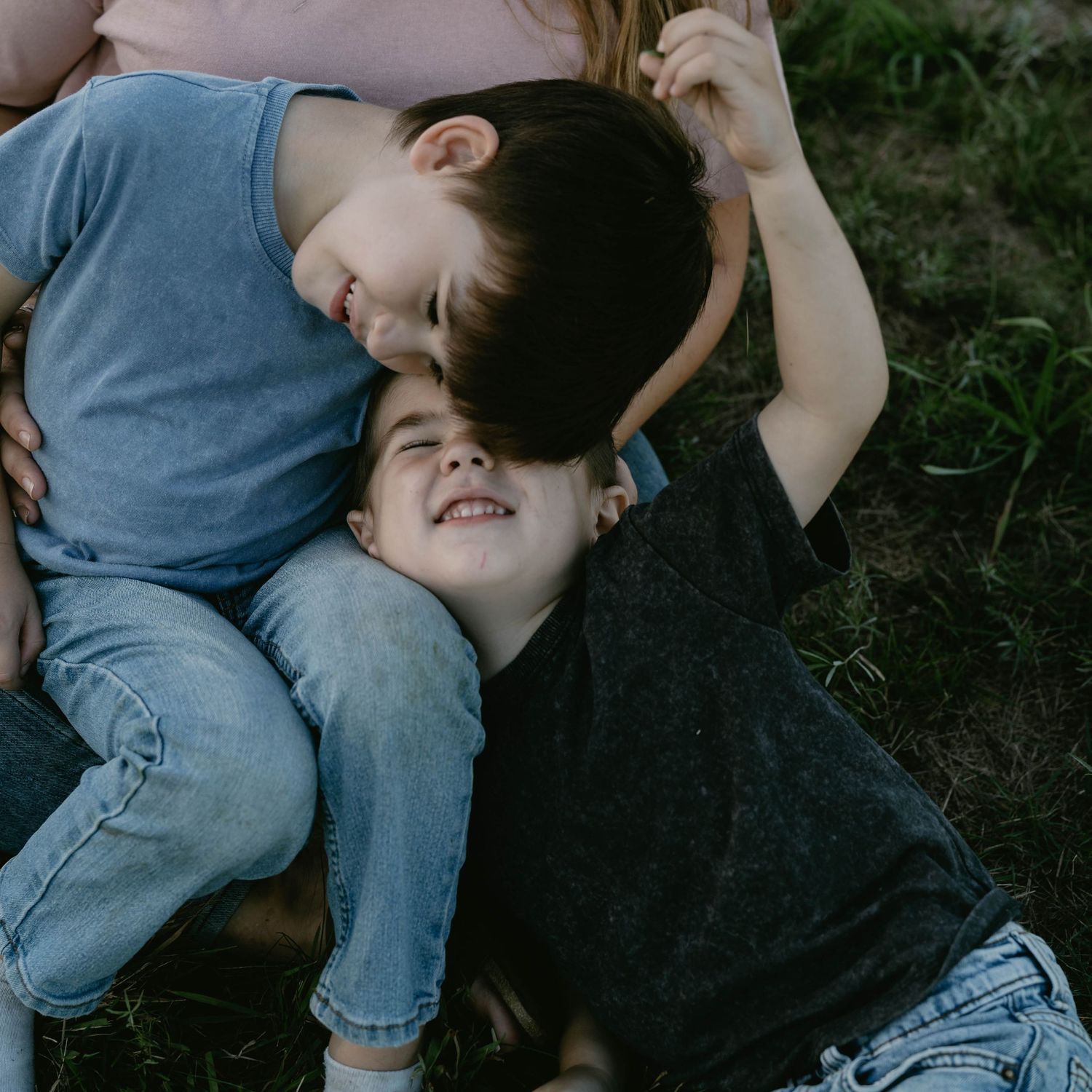 Two children lying on grass outdoors sharing a playful moment together on a sunny day.