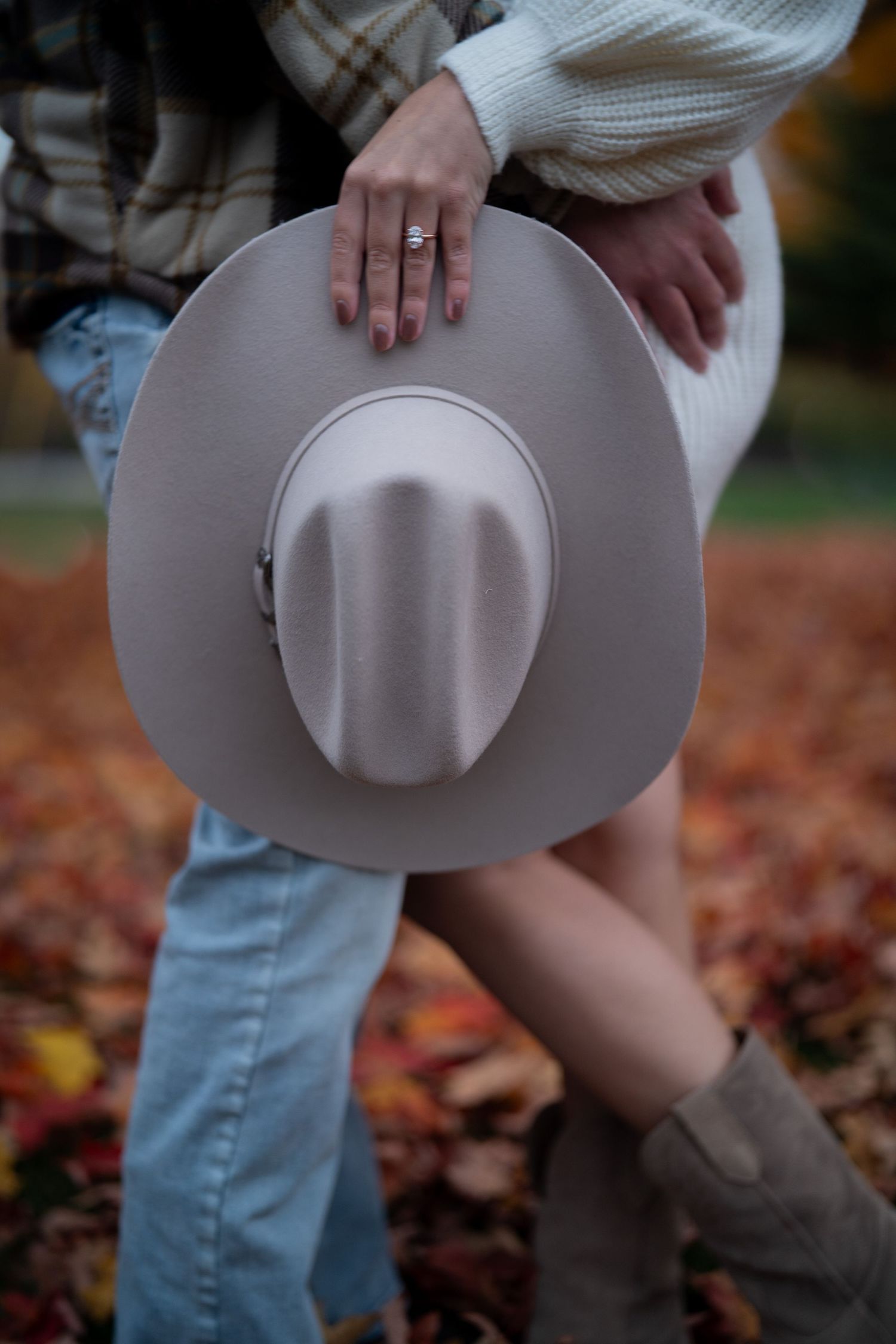 Close-up shot of hands holding a light-colored cowboy hat against a backdrop of autumn leaves.