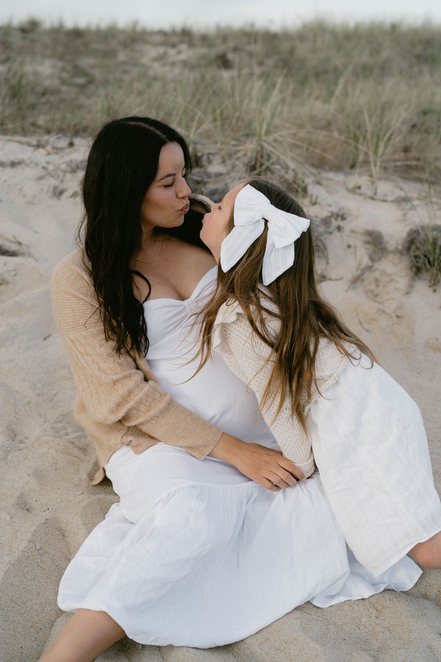 Intimate beach photoshoot featuring two people in flowing white dresses.