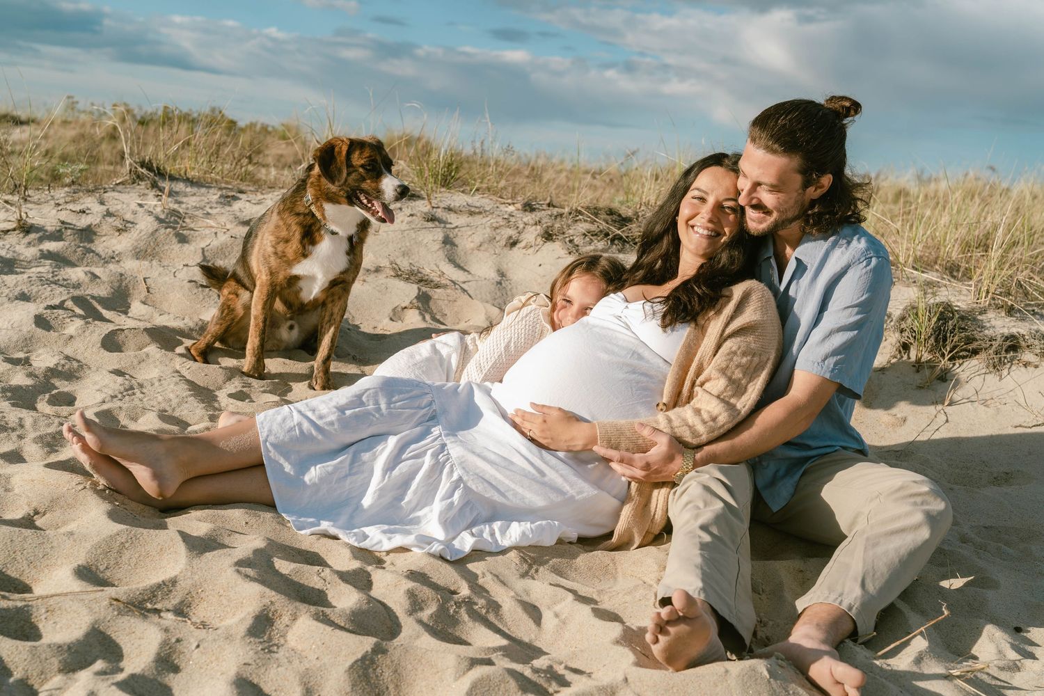 Family and dog relaxing together on a sandy beach during golden hour.