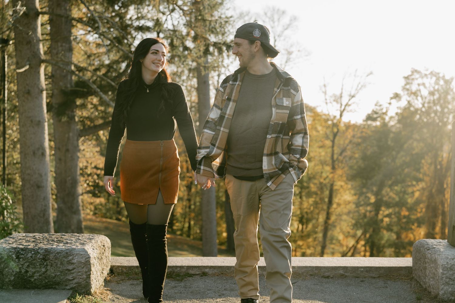 A couple shares a romantic moment while walking through a wooded area during sunset.