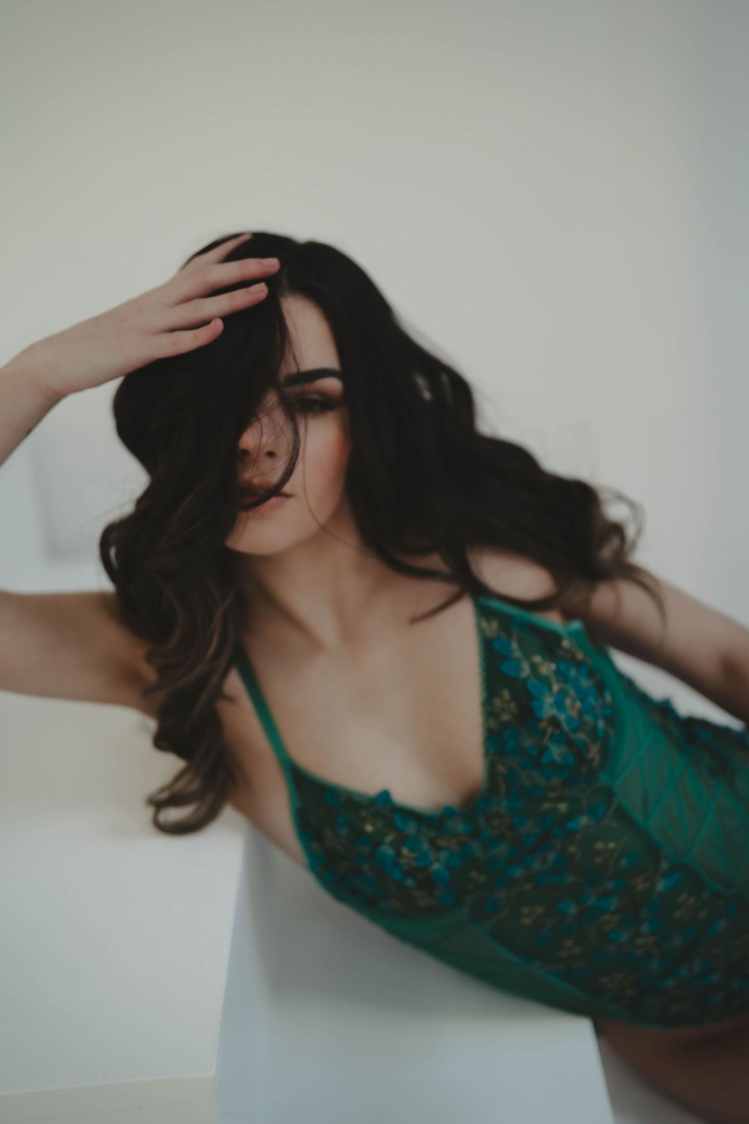 Dramatic hair movement captured in emerald lingerie against light background.