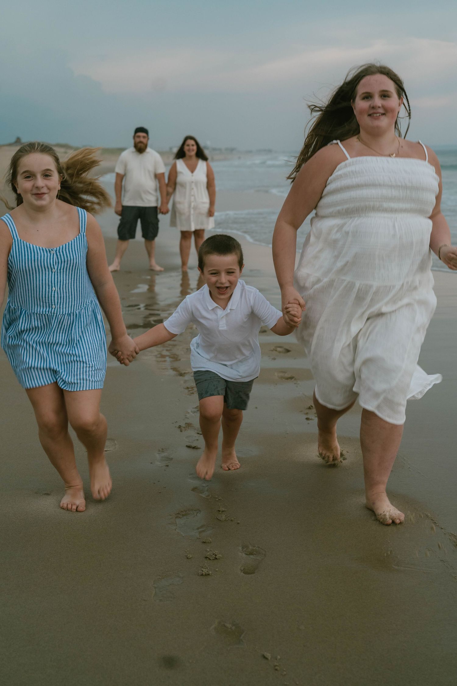 Family sitting on sand, smiling and enjoying a playful beach session.