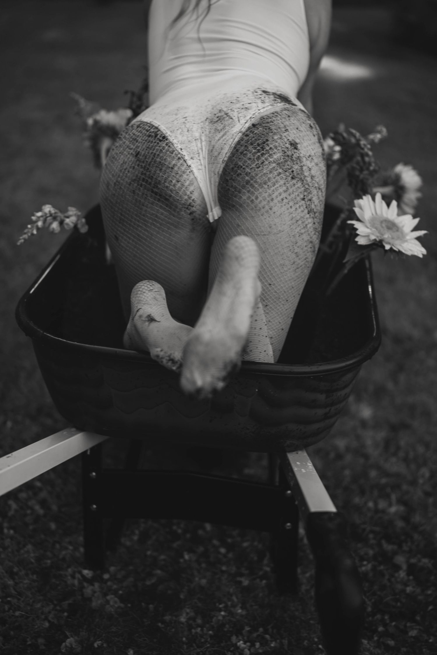 Black and white photo of someone sitting in a vintage suitcase with sunflowers.