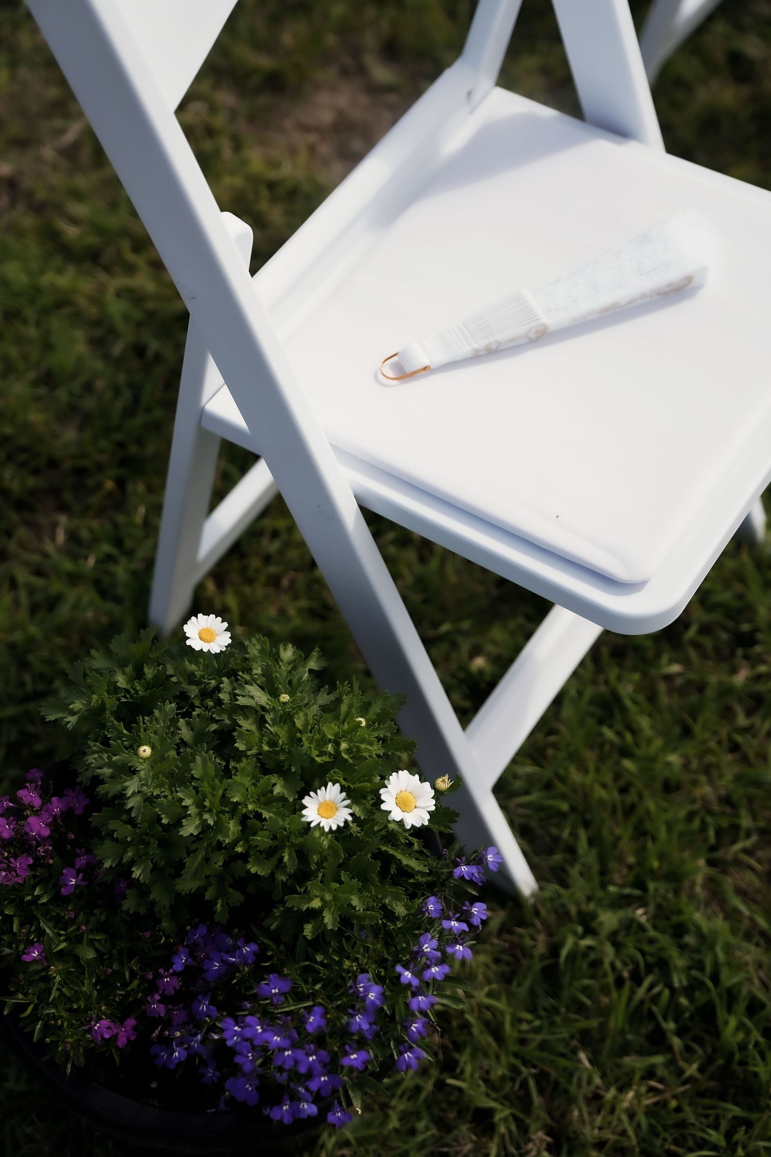 White folding chairs and purple flowers set up for an outdoor wedding ceremony.