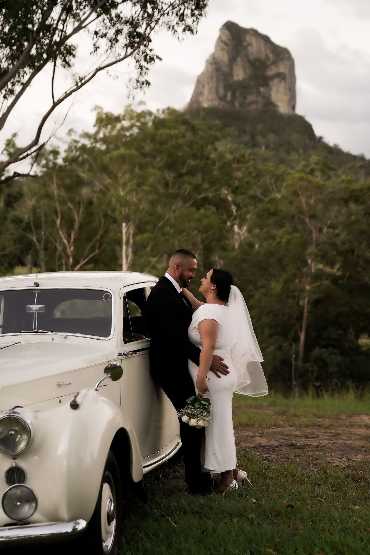 A classic white vintage Rolls Royce wedding car parked in front of a mountainous landscape.