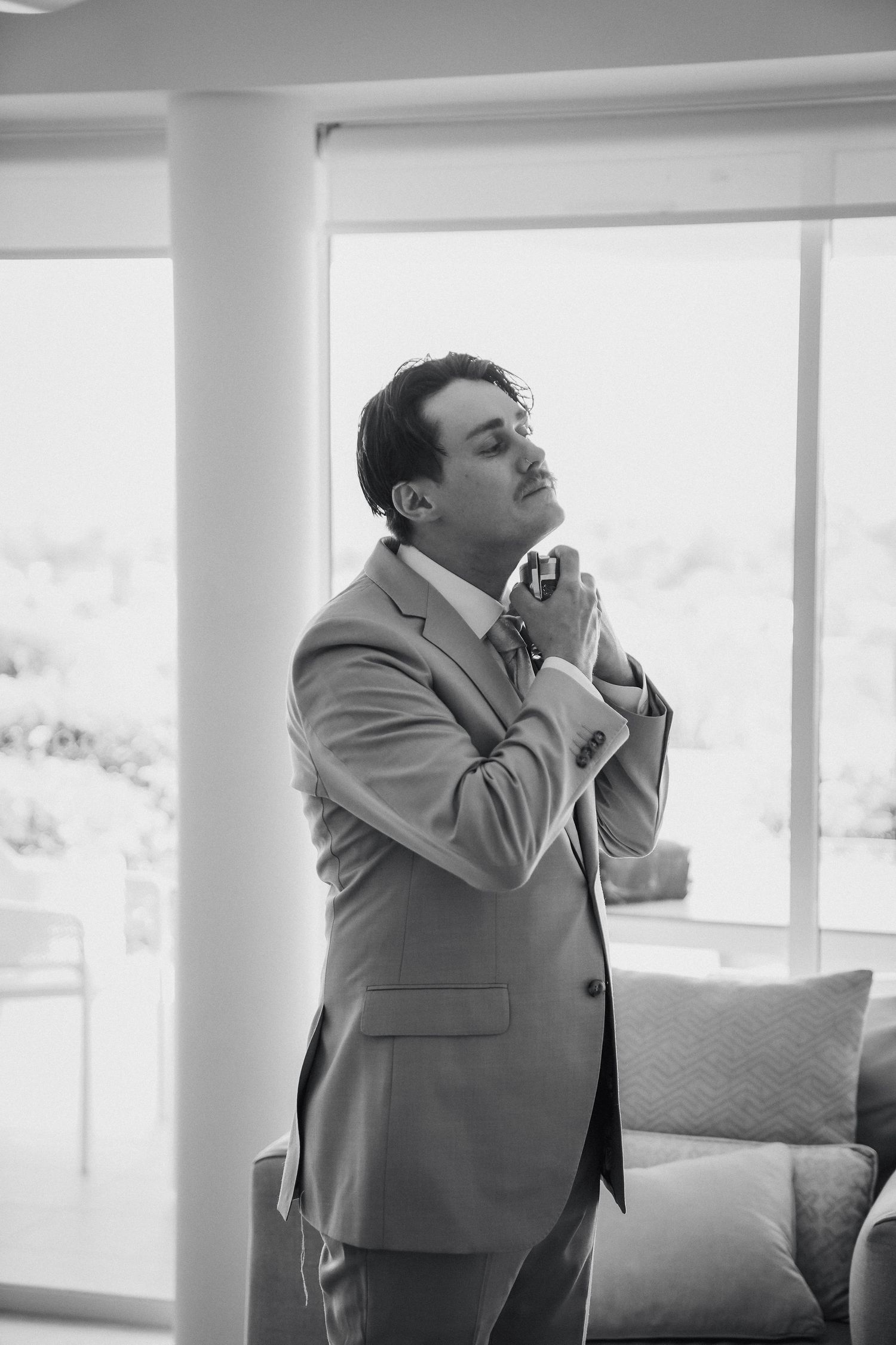 A person in a gray suit jacket stands by a window in a sequence of four similar black and white photos.