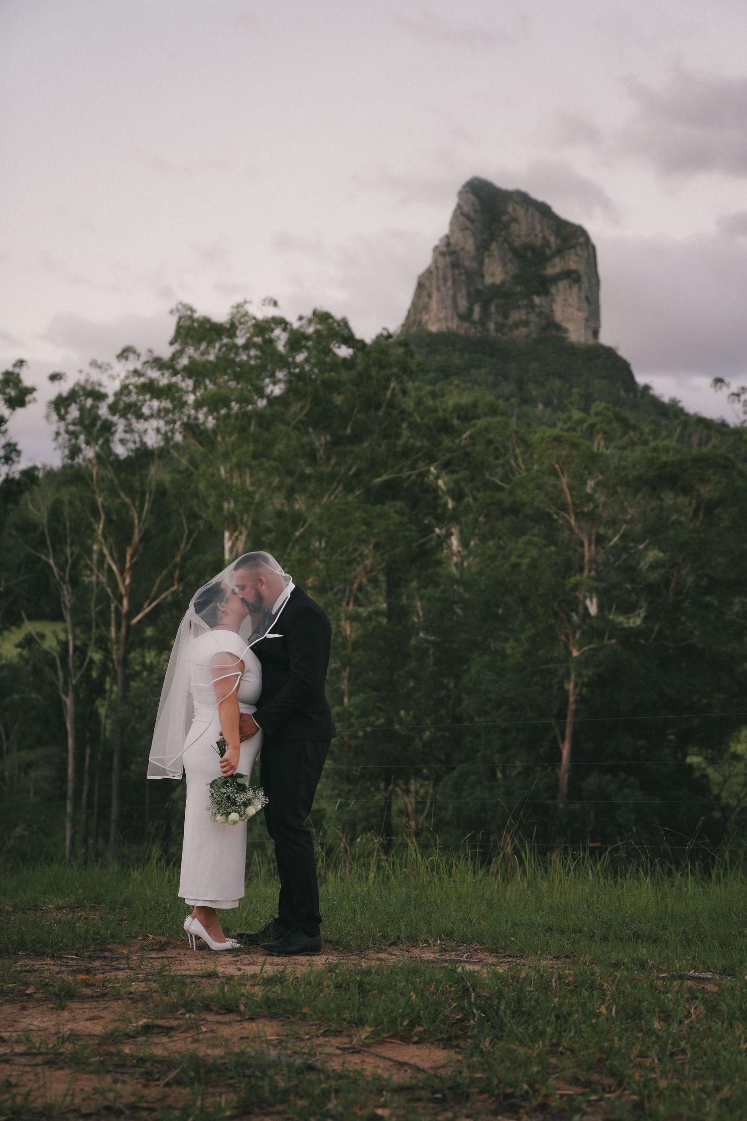 A couple shares an intimate moment during their wedding photoshoot with the dramatic Glass House Mountains as their backdrop.