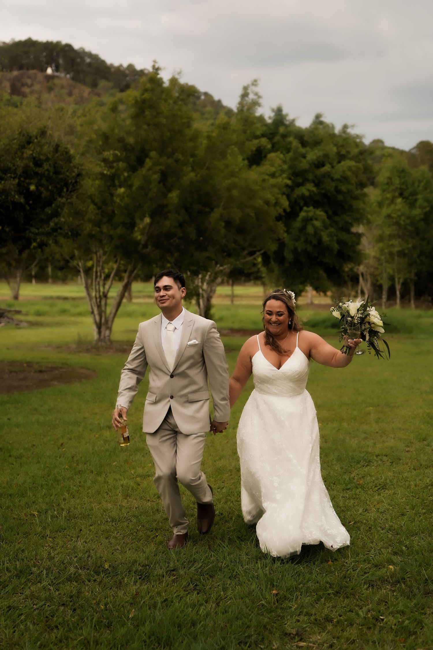 A joyful couple runs through a green field during their wedding photo session.