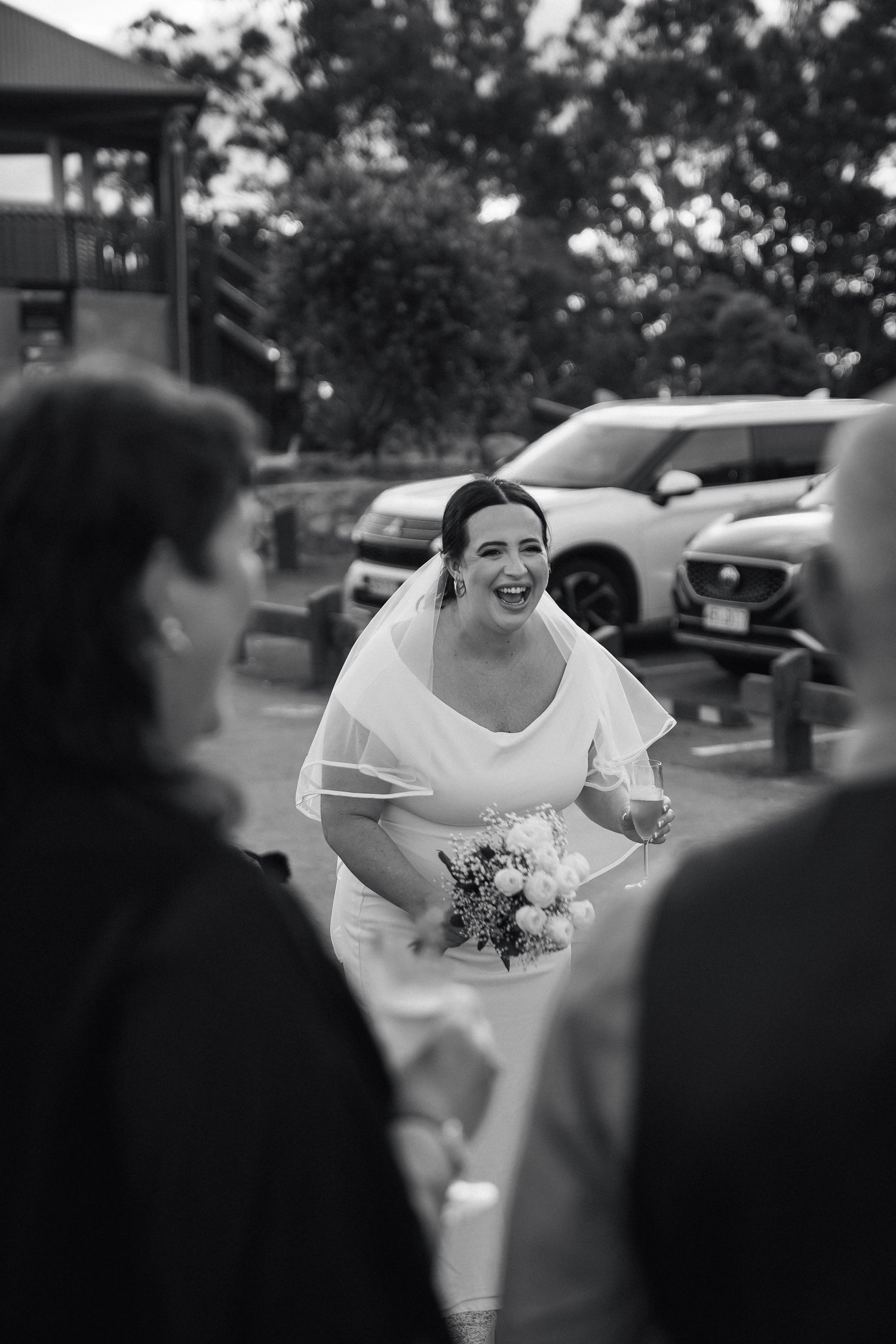 A candid black and white photo shows a joyful moment during a wedding celebration outdoors.