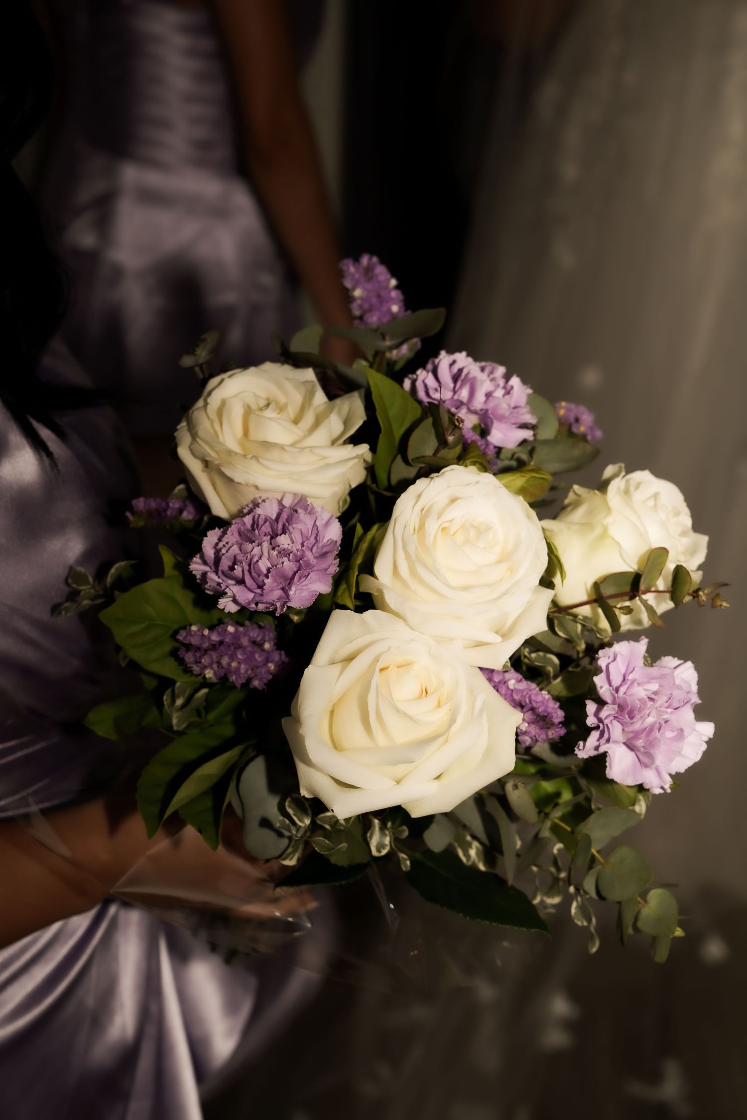 A romantic floral arrangement with white roses and purple flowers in dramatic lighting.