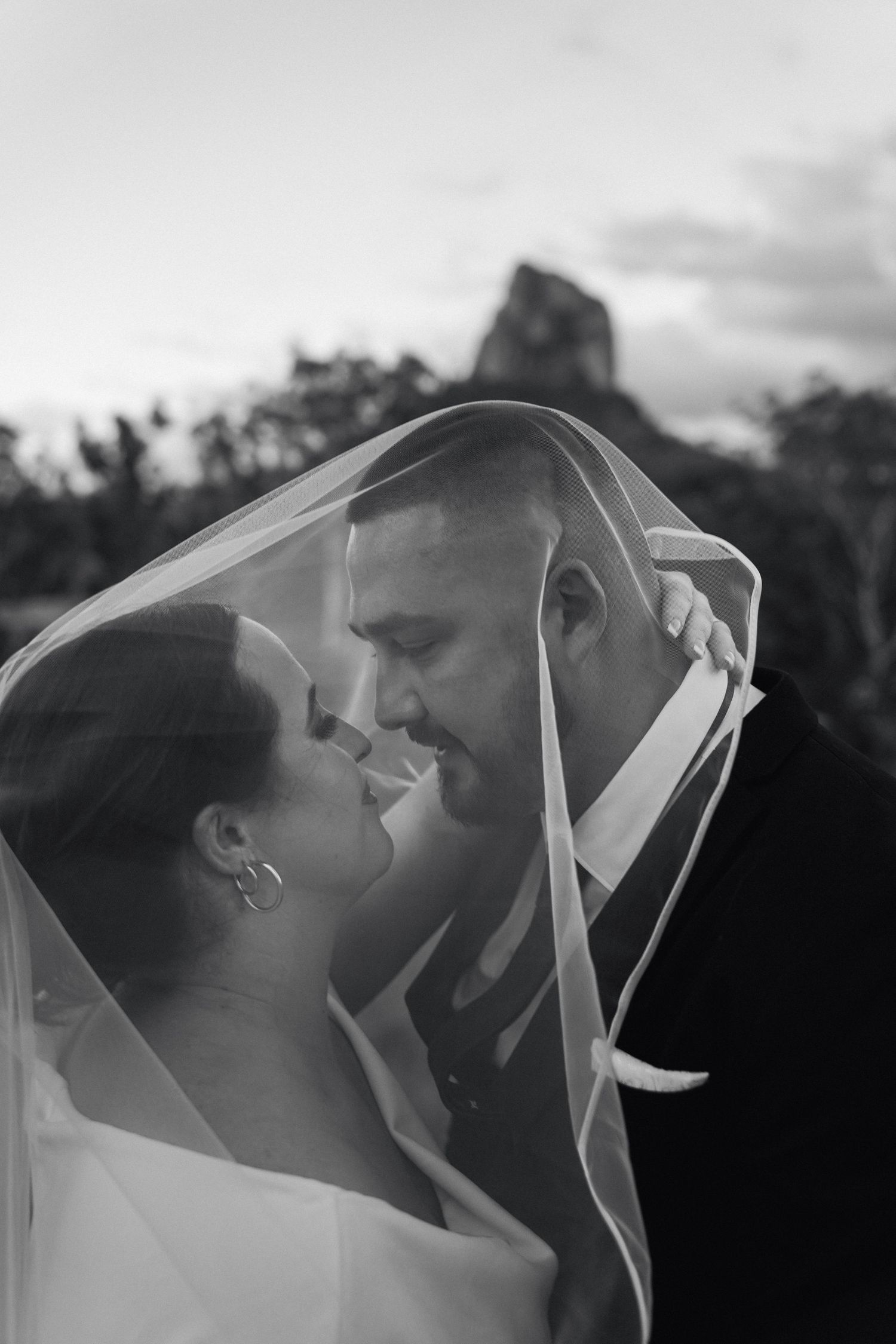 A romantic black and white wedding photo series showing a couple kissing under a delicate veil at sunset.