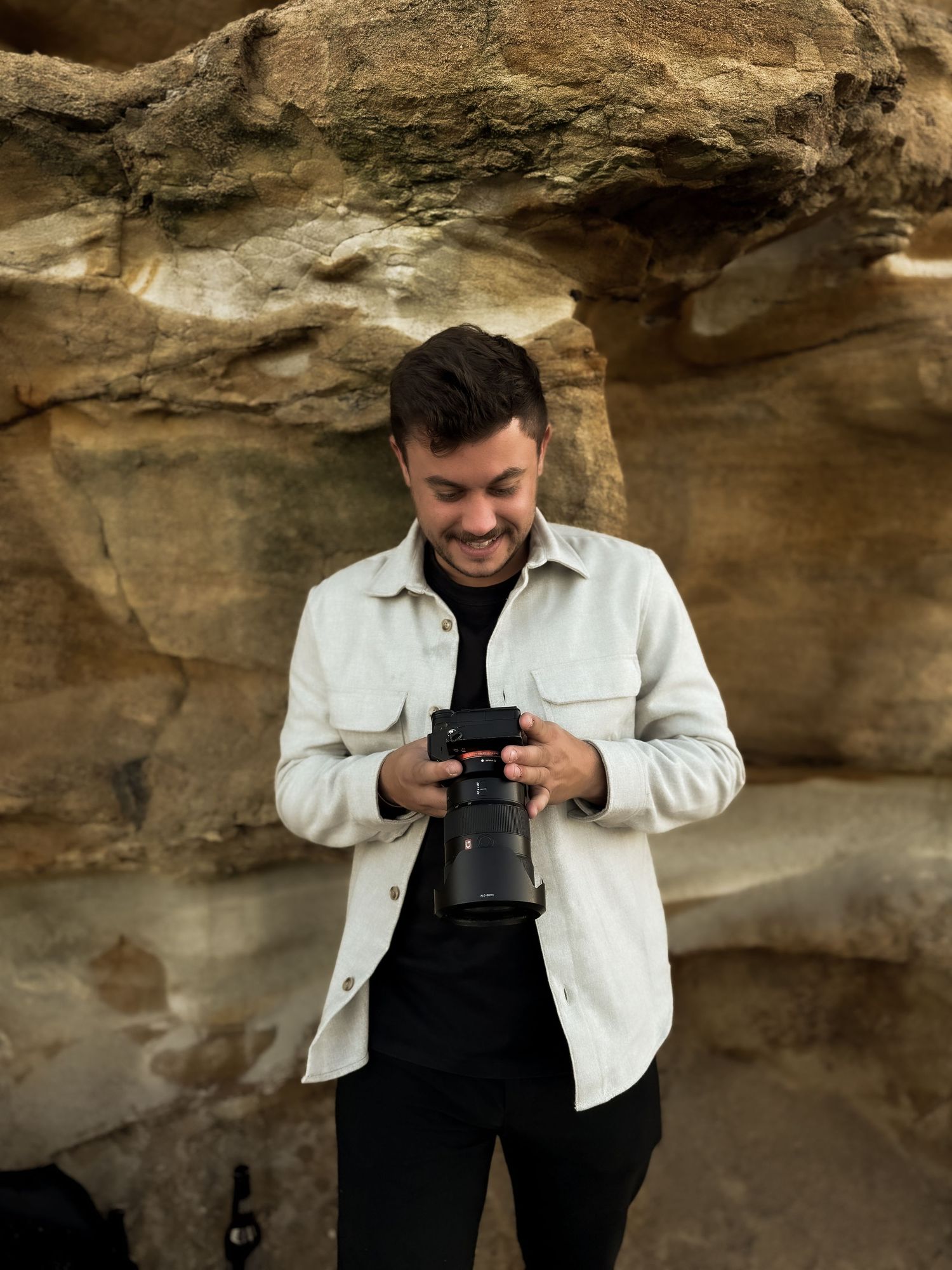 Someone in a white denim jacket and black outfit poses in a rocky cave setting.
