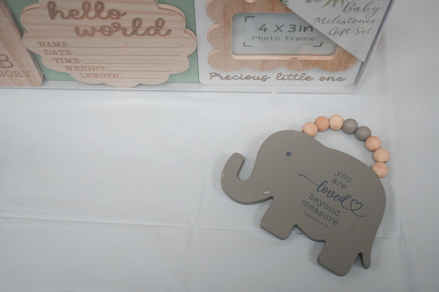 Gray elephant-shaped baby keepsake plaque with beaded ring, displayed alongside wooden nursery decor signs.