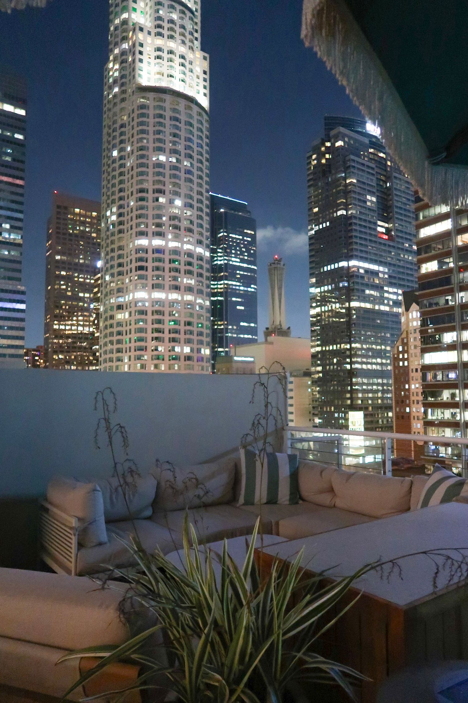 Modern city skyline at night with illuminated skyscrapers and a rooftop lounge area, travel photography, hotel photography, los angeles